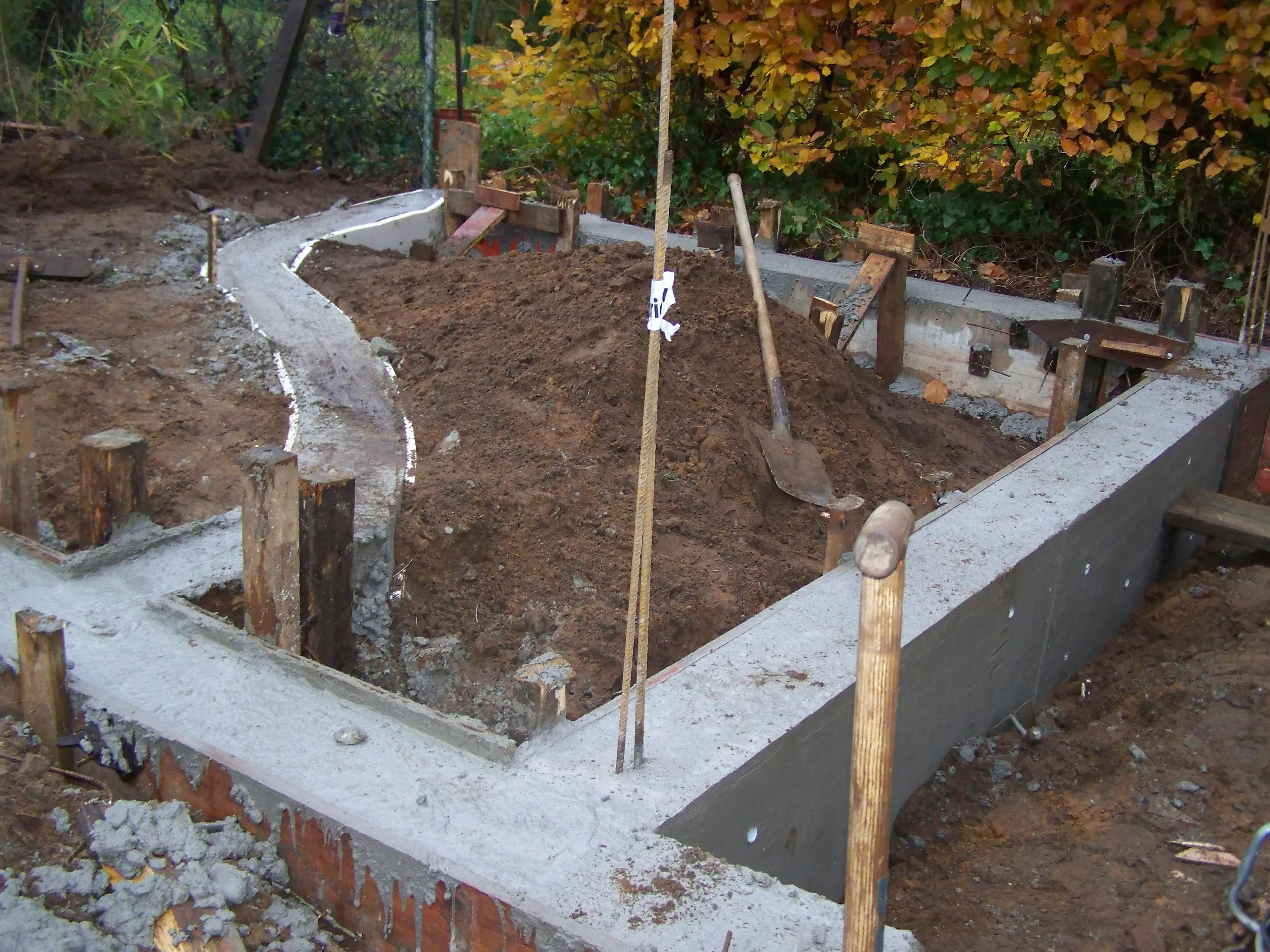 Fundament mit frischem Beton, Schalung und Baugrube im Rohbau auf herbstlicher Baustelle
