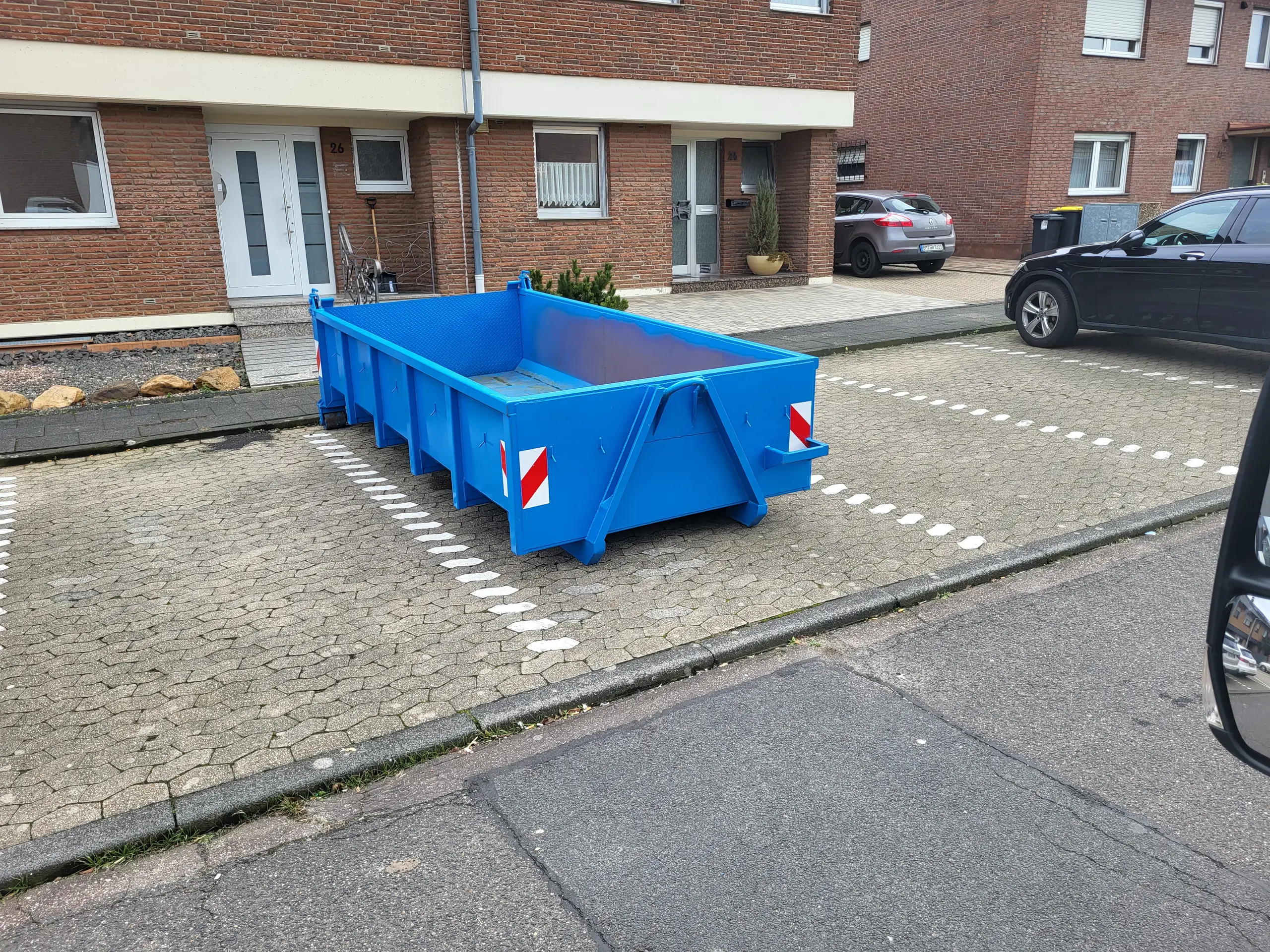 Blauer Absetzcontainer auf gepflastertem Stellplatz vor Wohngebäude als Containerdienst