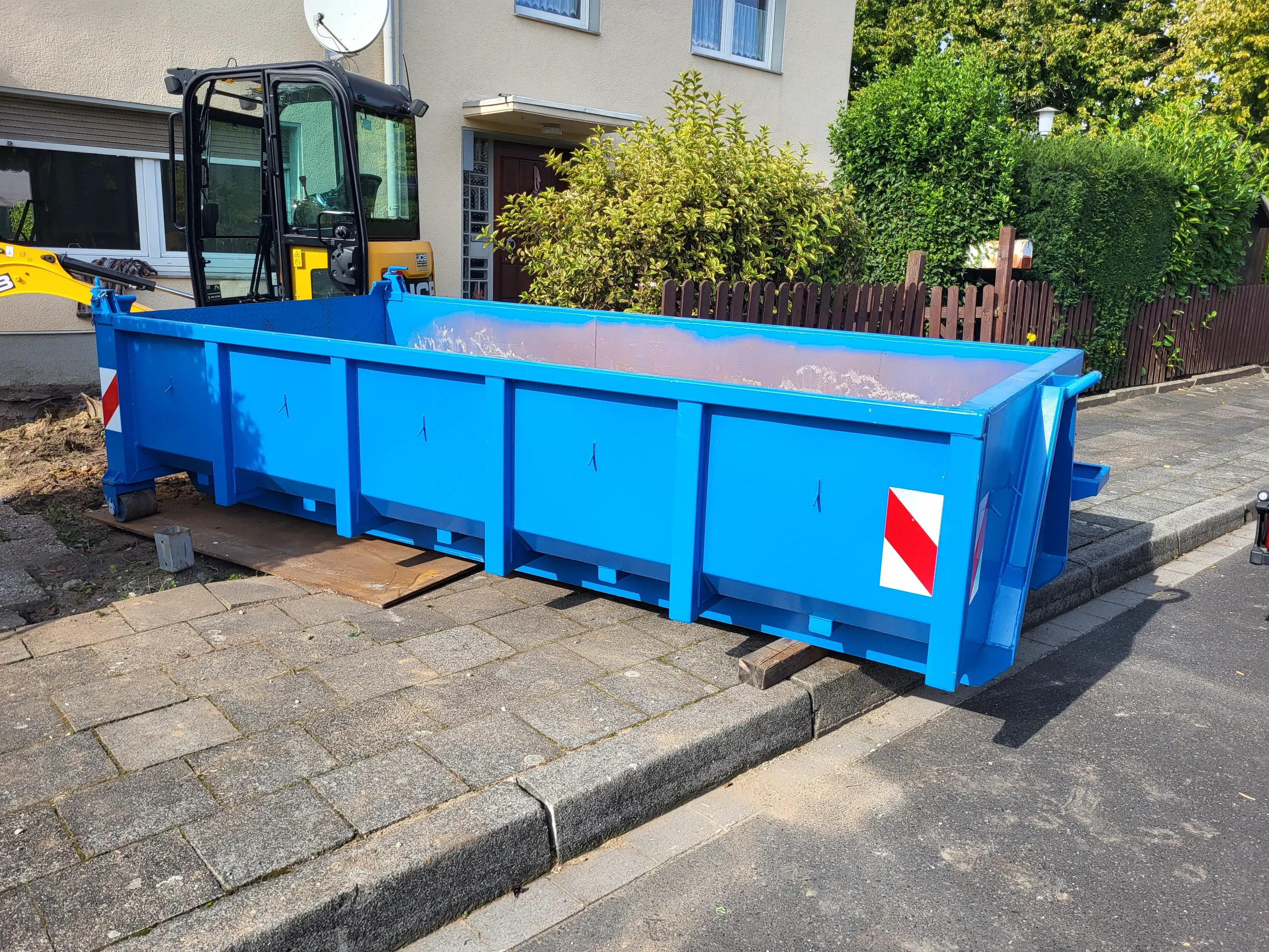 Blauer Absetzcontainer auf Pflaster vor Wohnhaus im Rahmen des Containerdienstes