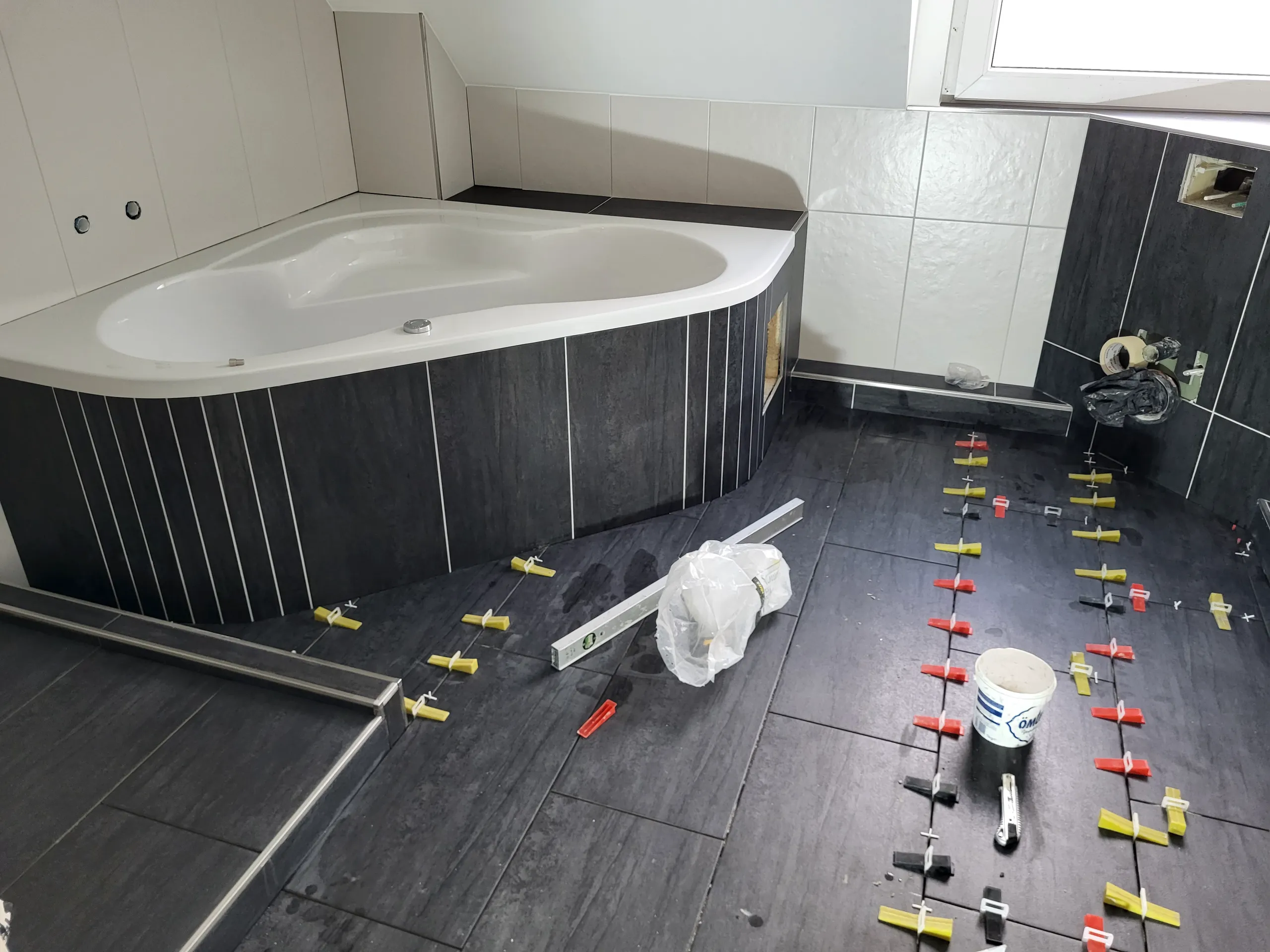 Schwarze Bodenfliesen werden mit Nivelliersystem vor einer Eckbadewanne verlegt