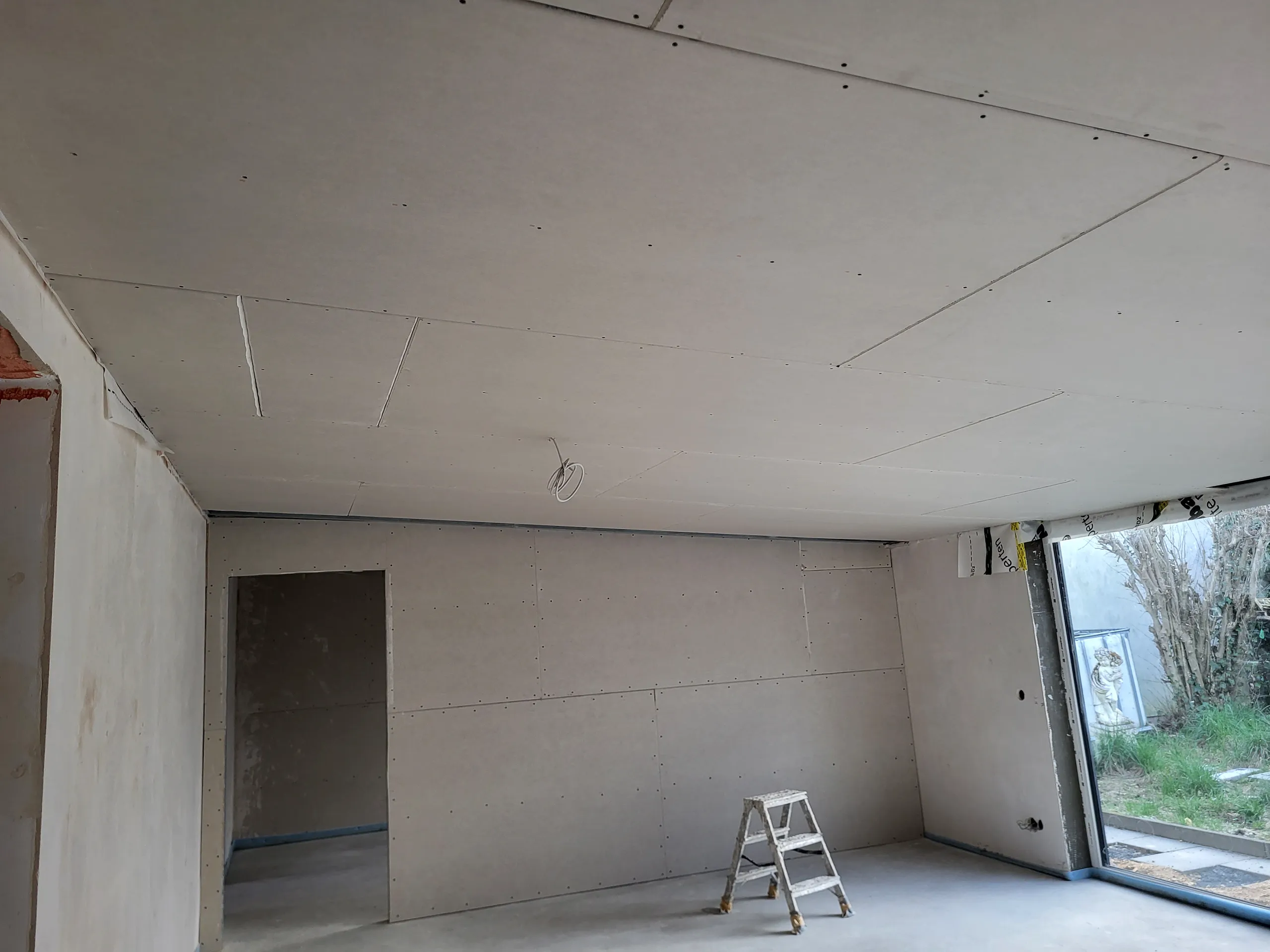 Innenansicht im Rohbau mit Trockenbauwänden und -decke aus Gipskarton, Estrichboden und freistehender Leiter