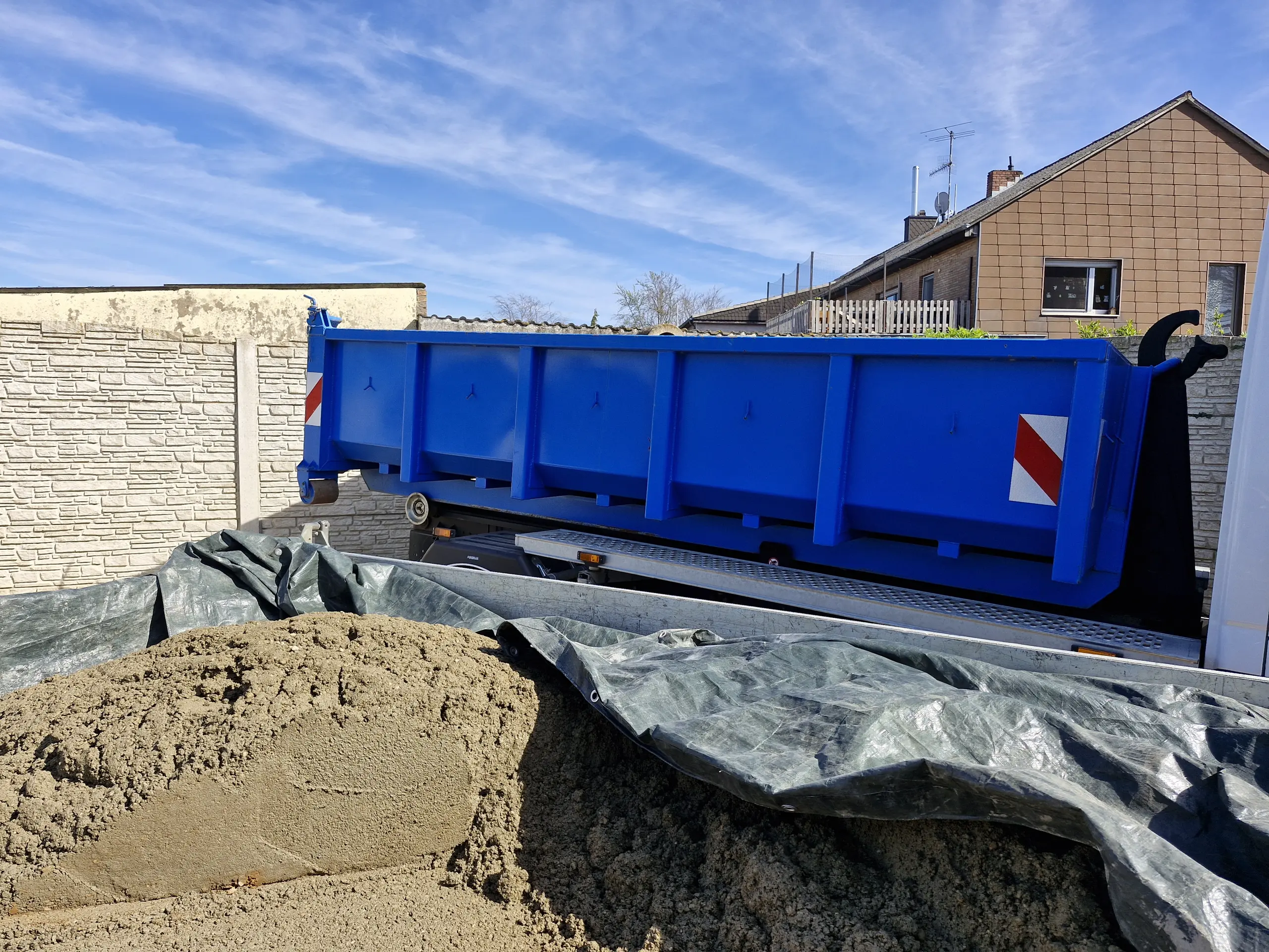 Blauer Abrollcontainer auf Lkw neben Sandhaufen für Containerdienst