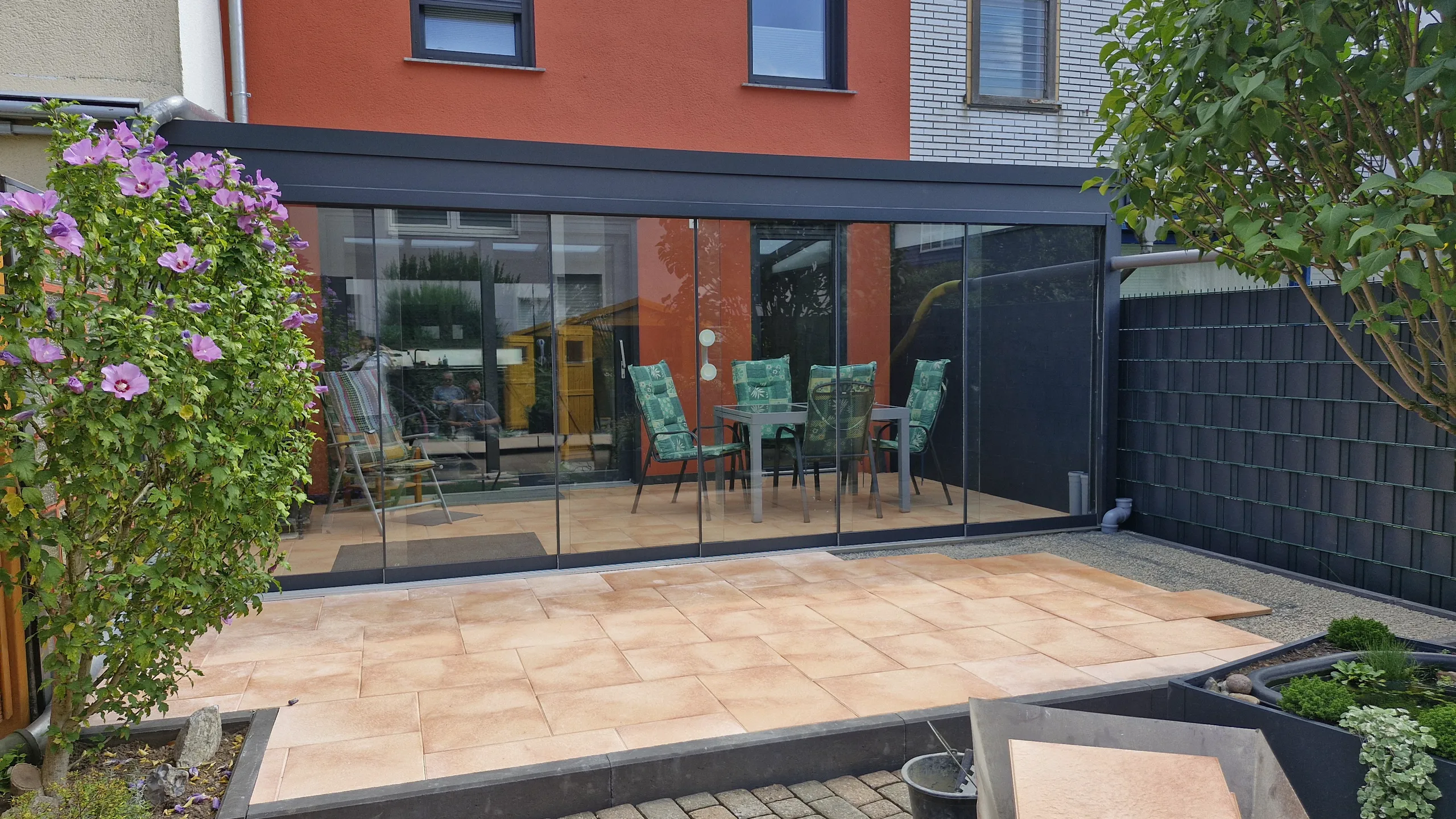 Terrassenbau mit Fliesenbelag und Glaswand: überdachte Sitzterrasse vor Einfamilienhaus