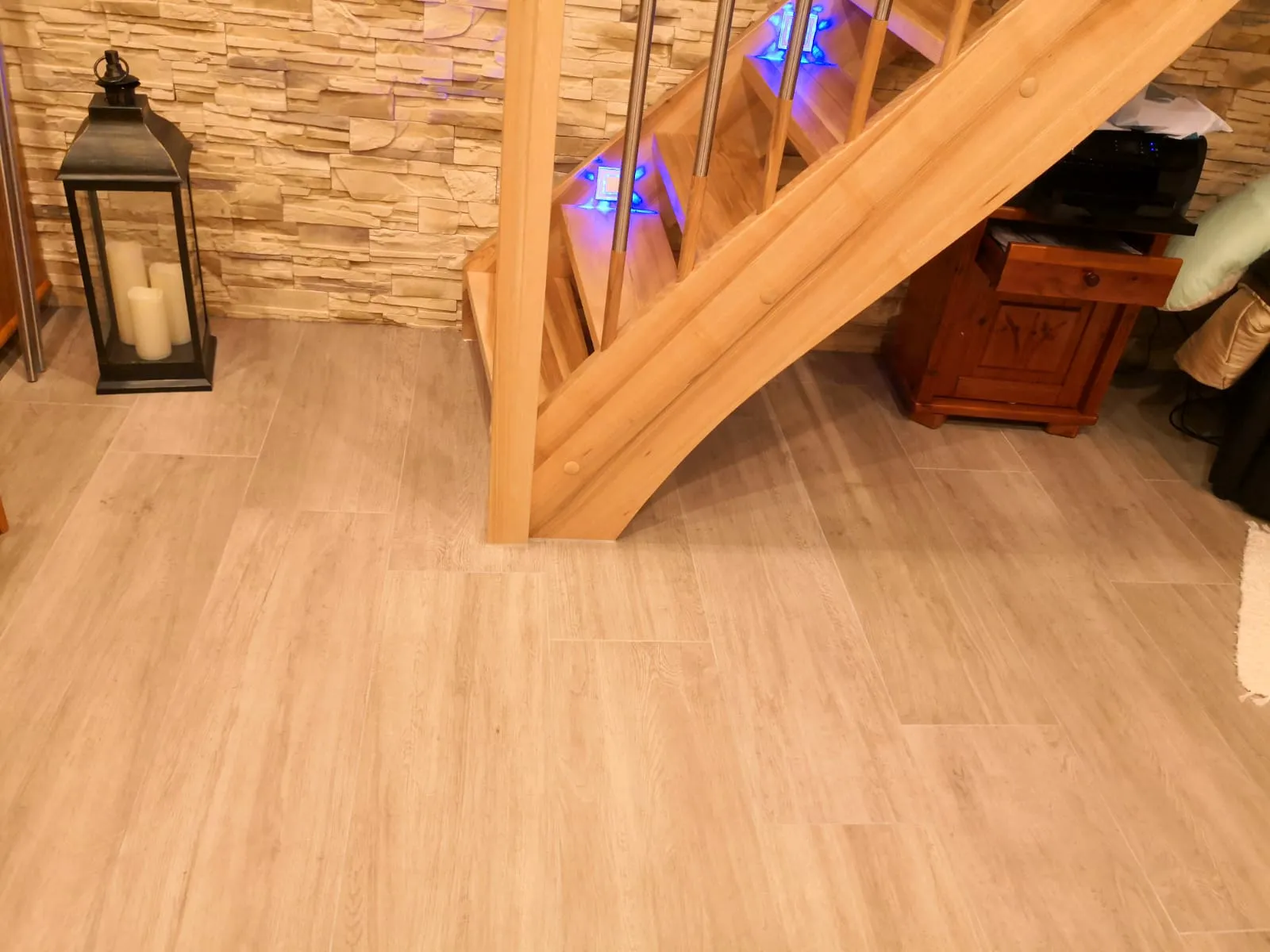 Holztreppe mit integrierten blauen LED-Stufenleuchten und Metallgeländer vor Dekorsteinwand