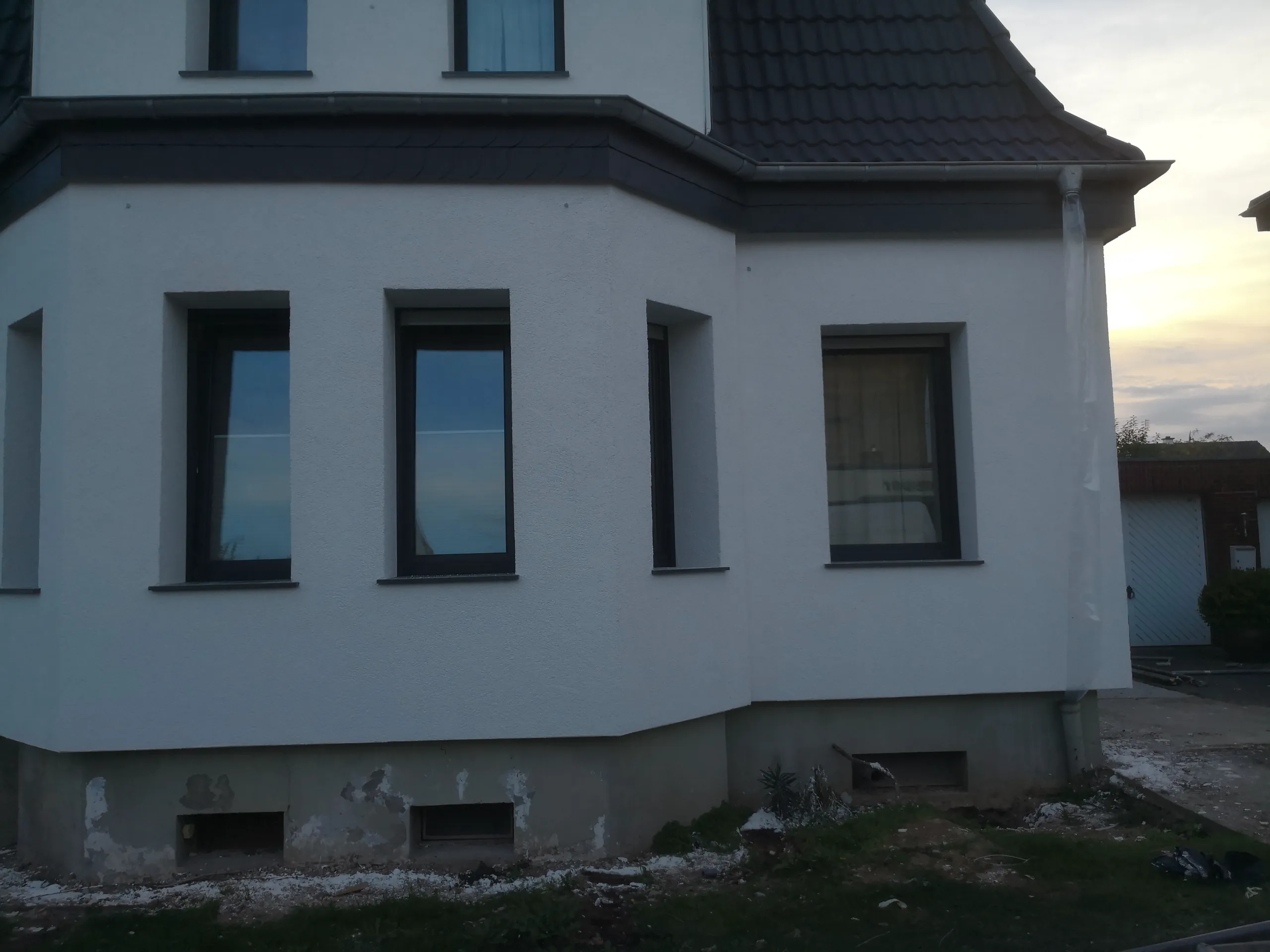 Weiß verputzte Hausfassade mit drei Fenstern und Bauabbruchresten Fassadensanierung