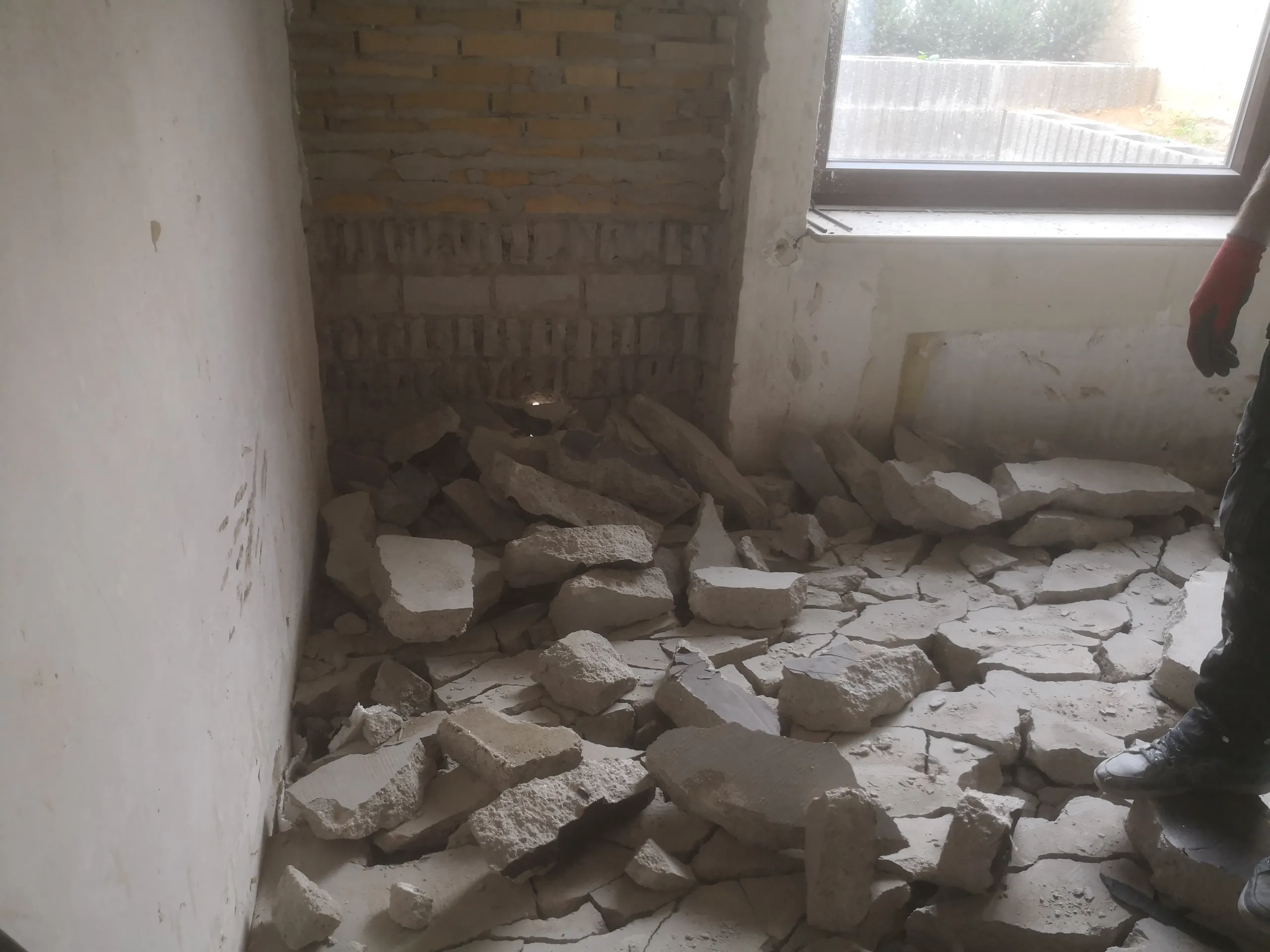 Innenraum mit aufgeworfenem Wand- und Betonschutt nach Abbrucharbeiten, Blick auf Fenster und Arbeiter mit Handschuhen im Hintergrund