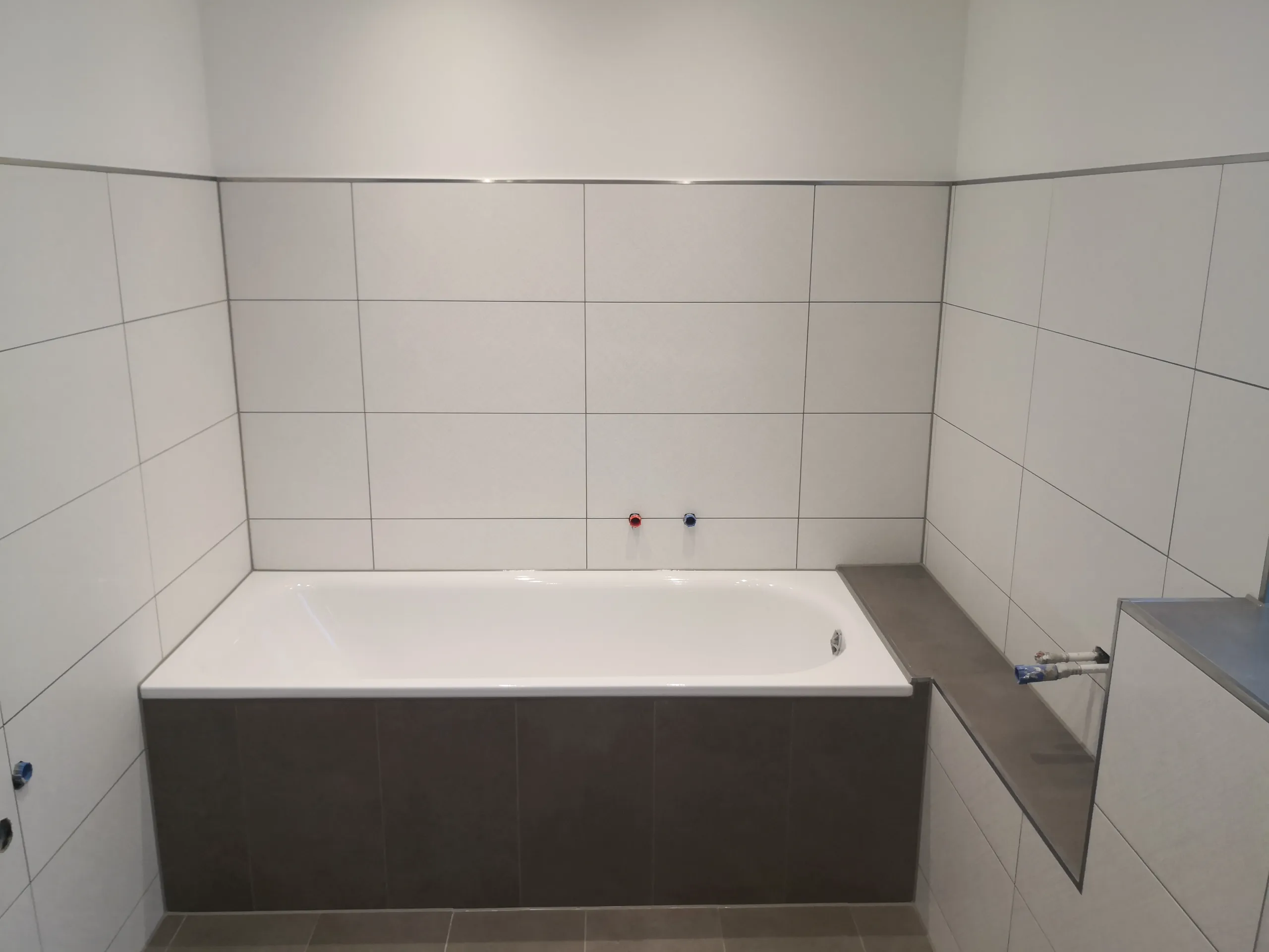 Neuer Wannenbereich mit weißen Wandfliesen und grauem Sockel im Rahmen einer Badsanierung
