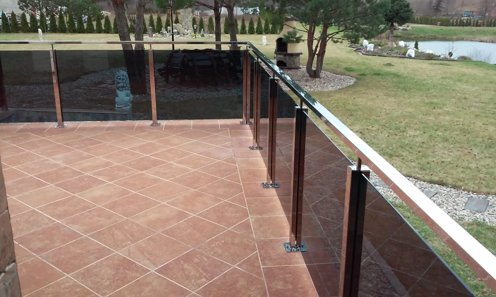 Glasgeländer auf Terrasse mit Edelstahlpfosten und keramischen Fliesen und Gartenblick