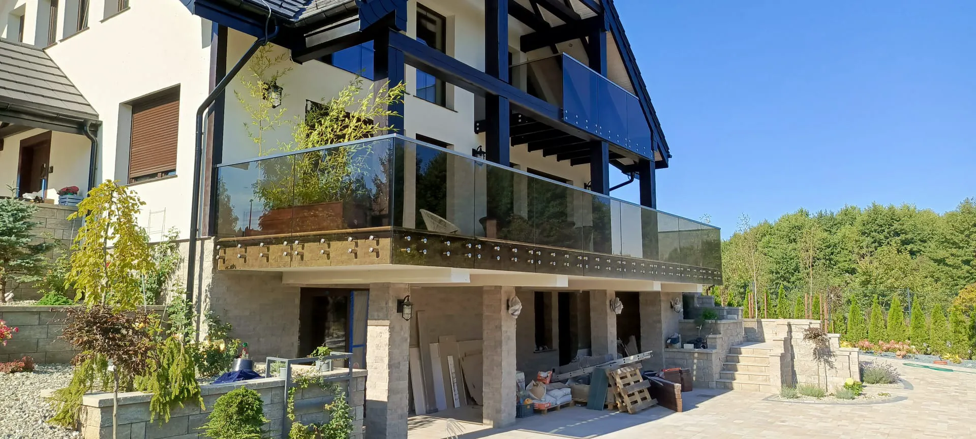 Modernes Glasgeländer am Balkon über gepflasterter Terrasse und Baustellenmaterial