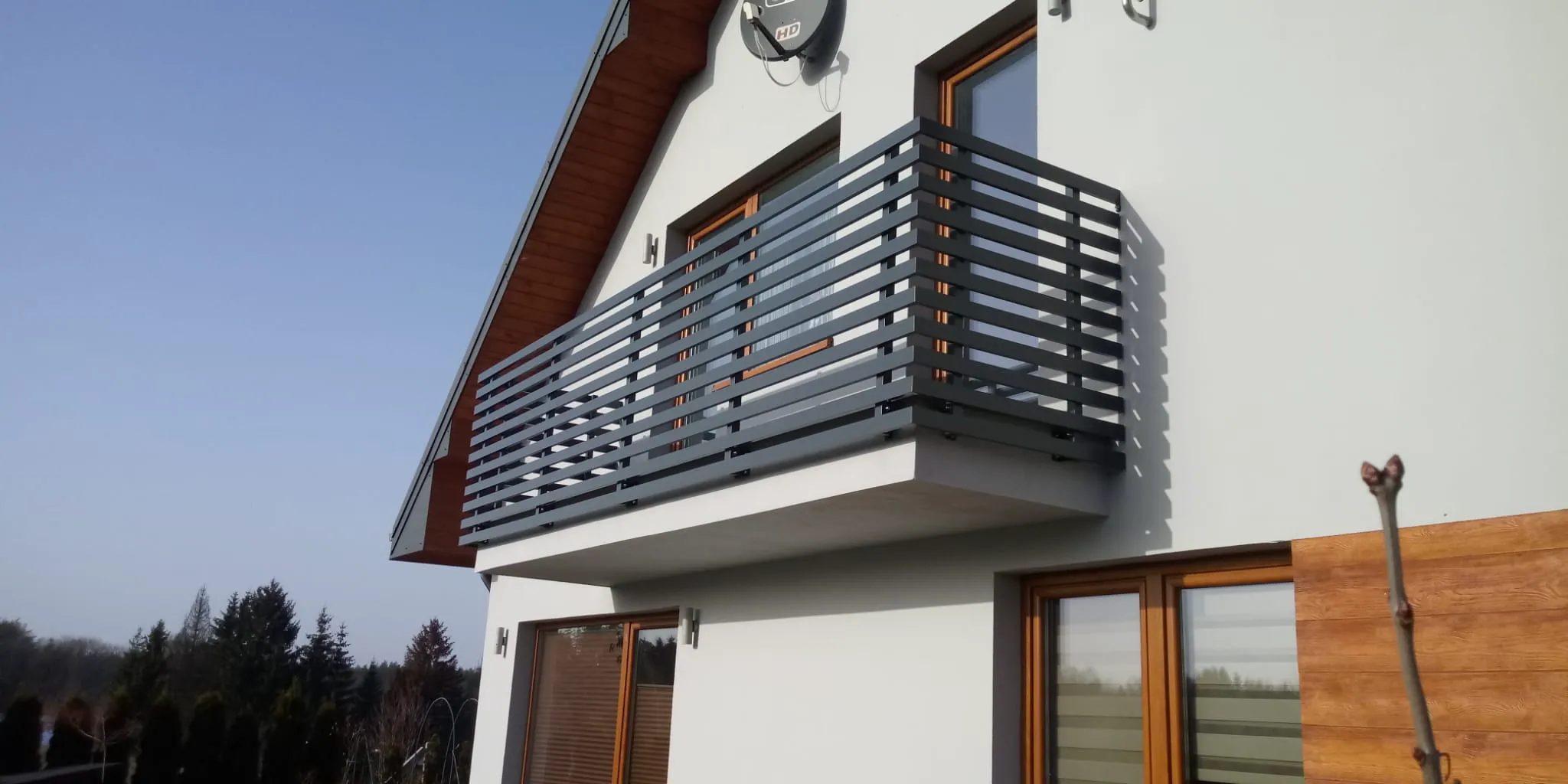 Weiß verputzte Hausfassade mit Holzfenstern und grauem Metallgeländer am Balkon