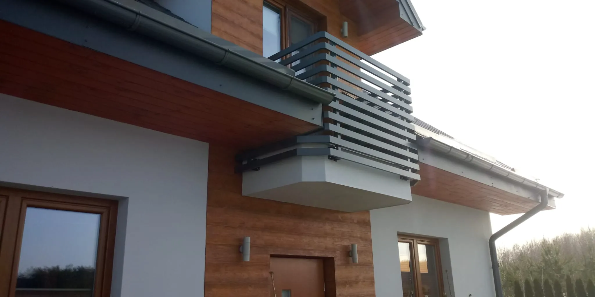 Moderner Hausaußenbereich mit kleinem Balkon und Metallgeländer, Holzverkleidung und Fenstern