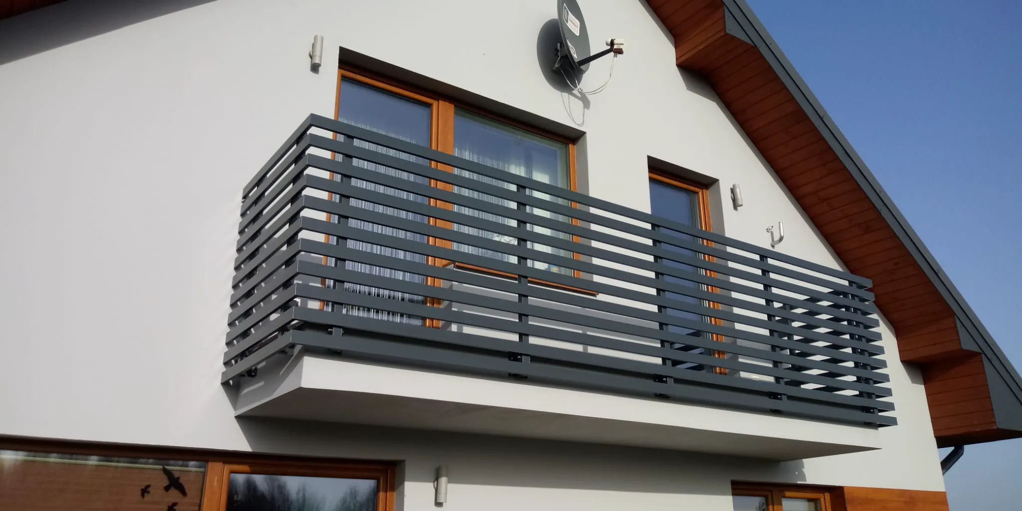 Balkon mit Metallgeländer und Holzfenstern an weißer Fassade