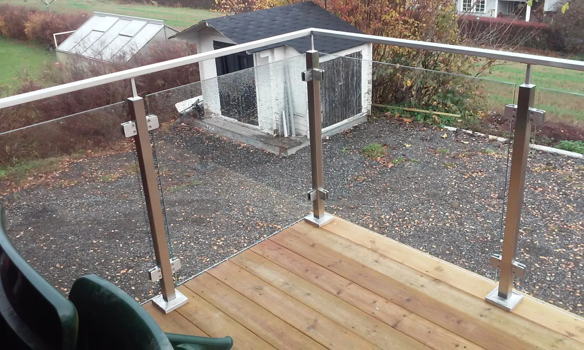 Balkon mit neu montiertem Glasgeländer auf Holzterrasse und Blick auf Schuppen und Garten