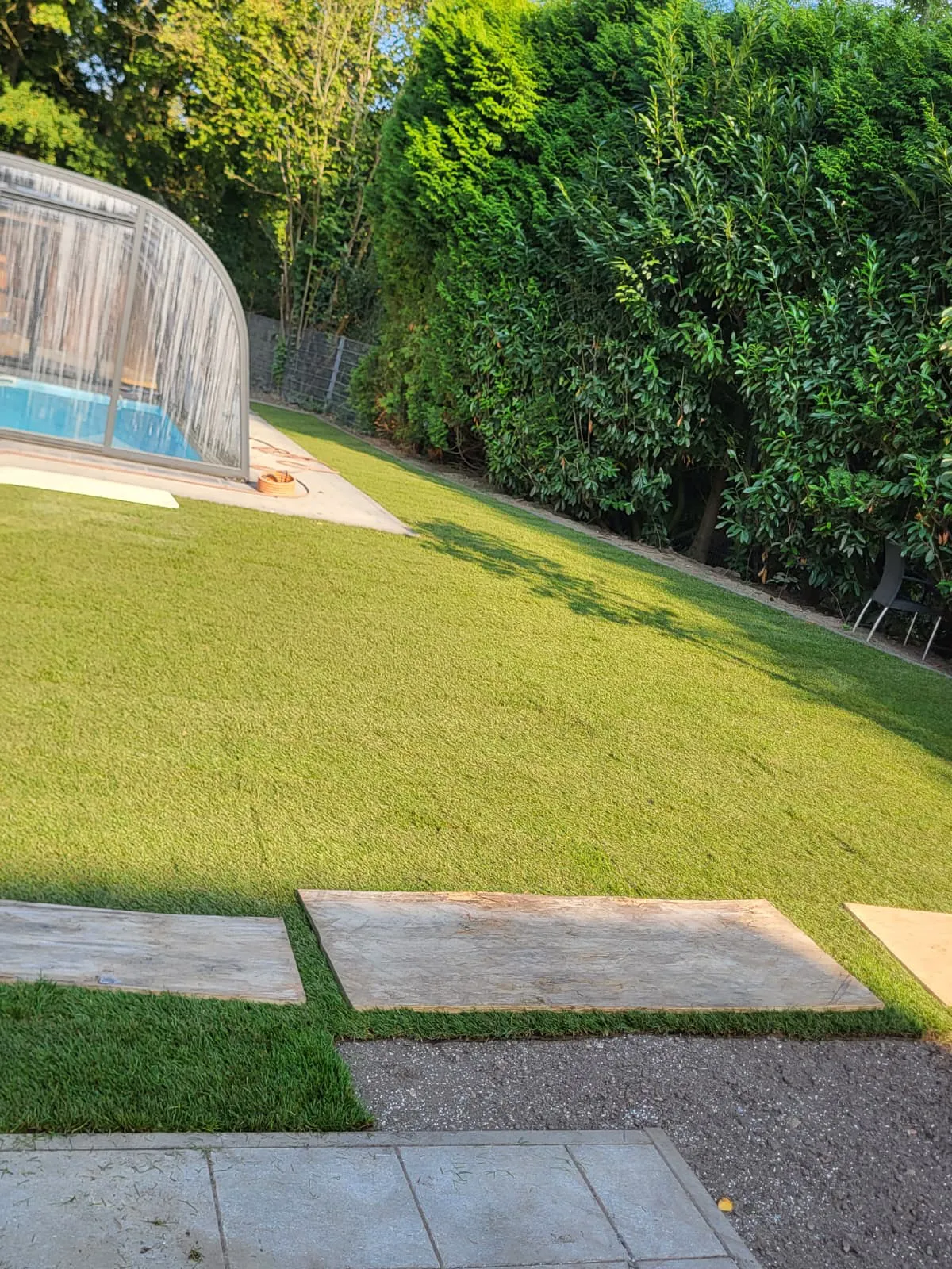 Neu angelegter Rasen mit Betonplatten und Poolüberdachung im Hintergrund