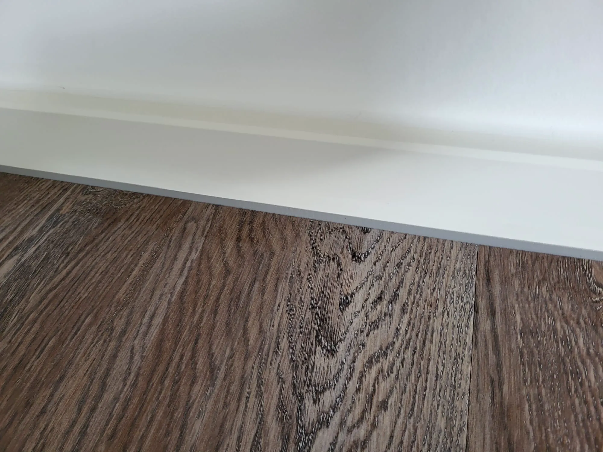 Dunkler Laminatboden mit weißer Sockelleiste an Wand, Laminat verlegen