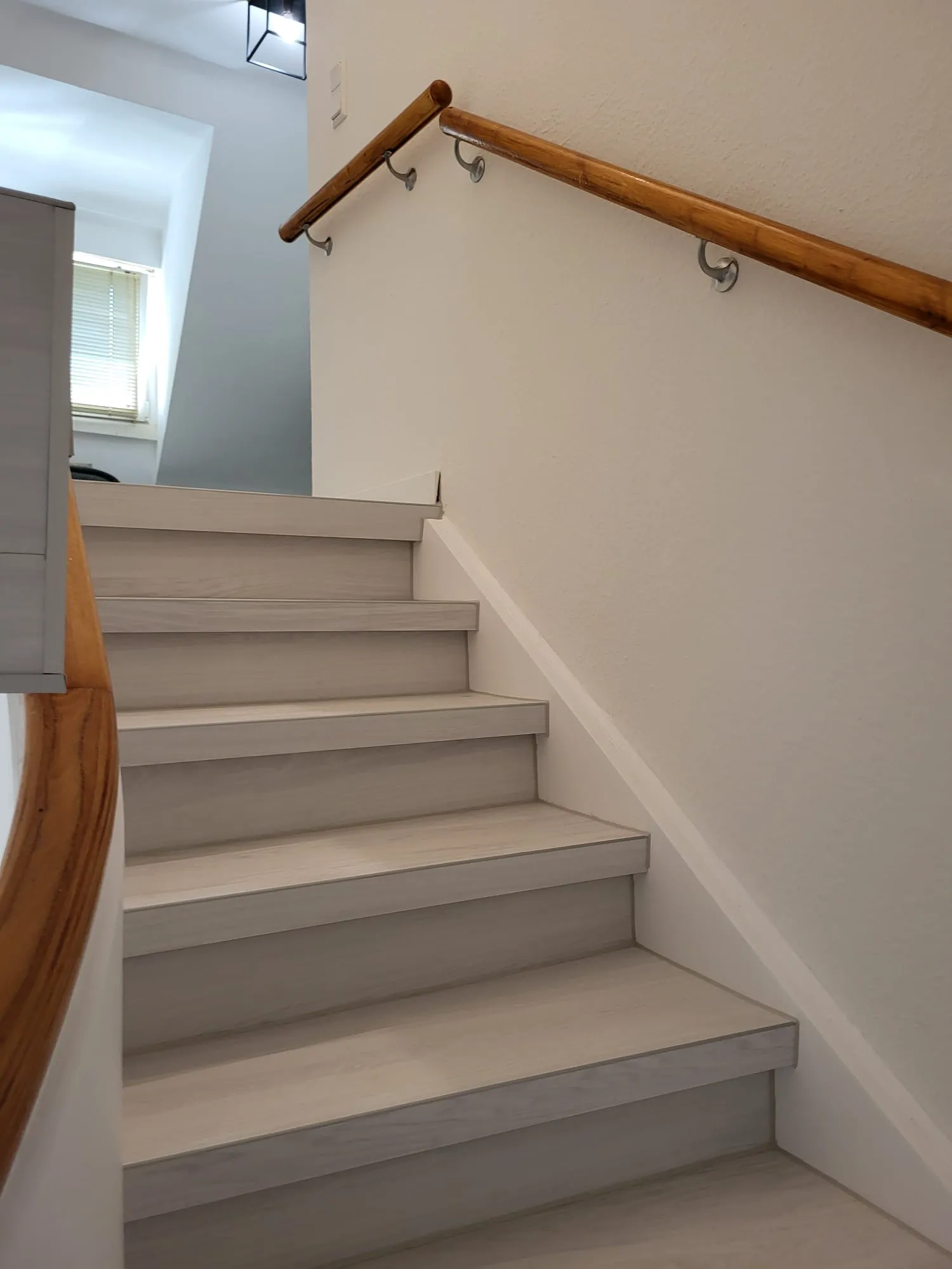 Moderne Holztreppe mit weiß lasierten Stufen und seitlichem Holzgeländer im Innenbereich
