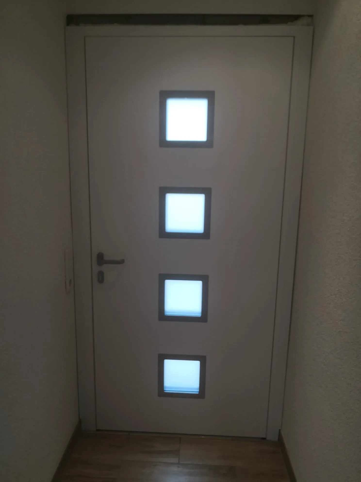 Innentüren: Weiße Tür mit vier quadratischen satinierten Fenstern in schmalem Flur und Holzfußboden