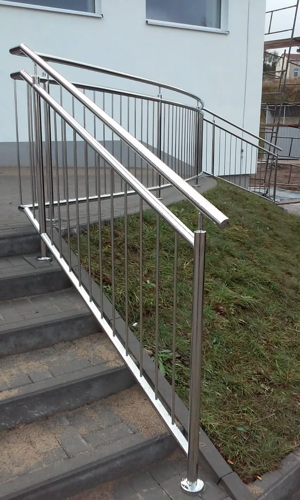 Metallgeländer aus Edelstahl an Außentreppe und barrierefreier Rampe neben weißem Gebäude