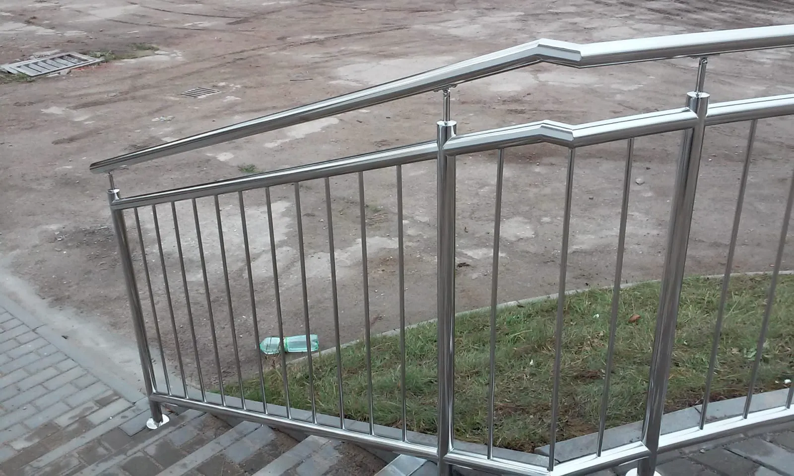 Metallgeländer aus Edelstahl an Treppe auf Pflasterfläche neben Grünfläche