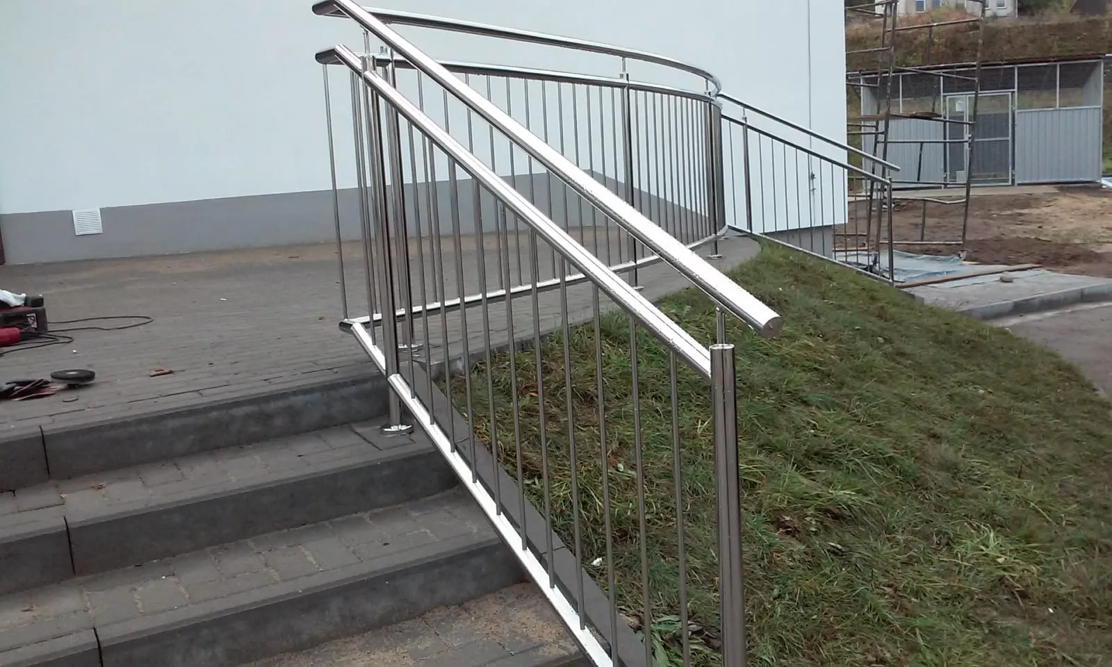 Außentreppenaufgang mit Metallgeländer aus Edelstahl neben gepflasterter Fläche und Grünanlage