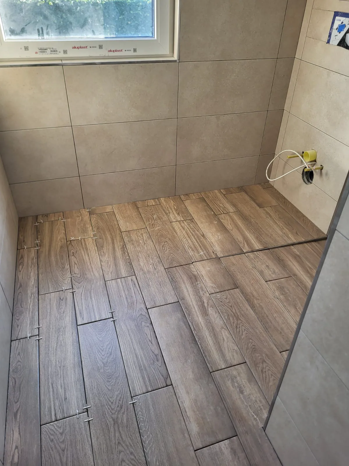 Halbfertige Fliesenverlegung mit Holzoptik-Bodenplatten und Wandfliesen im Badezimmer