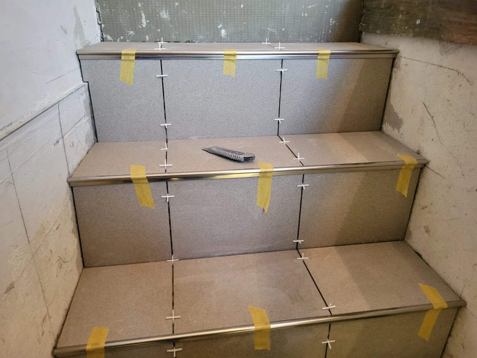 Graue Treppenstufen im Rohbau mit Fliesenkreuzen und Aluminium-Aufsatzprofilen beim Fliesen verlegen