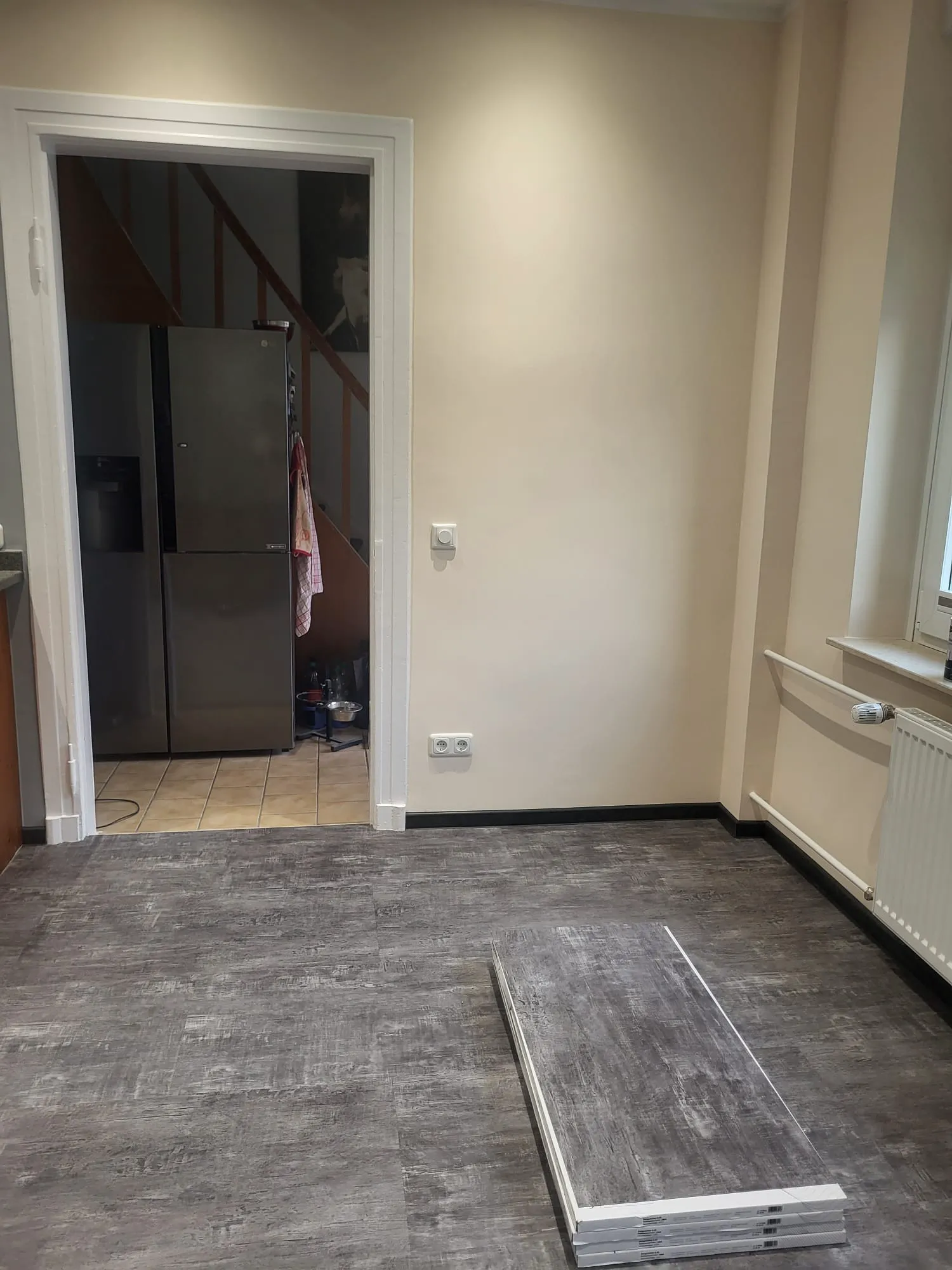 Dunkler Vinylboden im Wohnraum mit aufgestapelten Paneelen vor offener Küchentür, kurz vor der Verlegung
