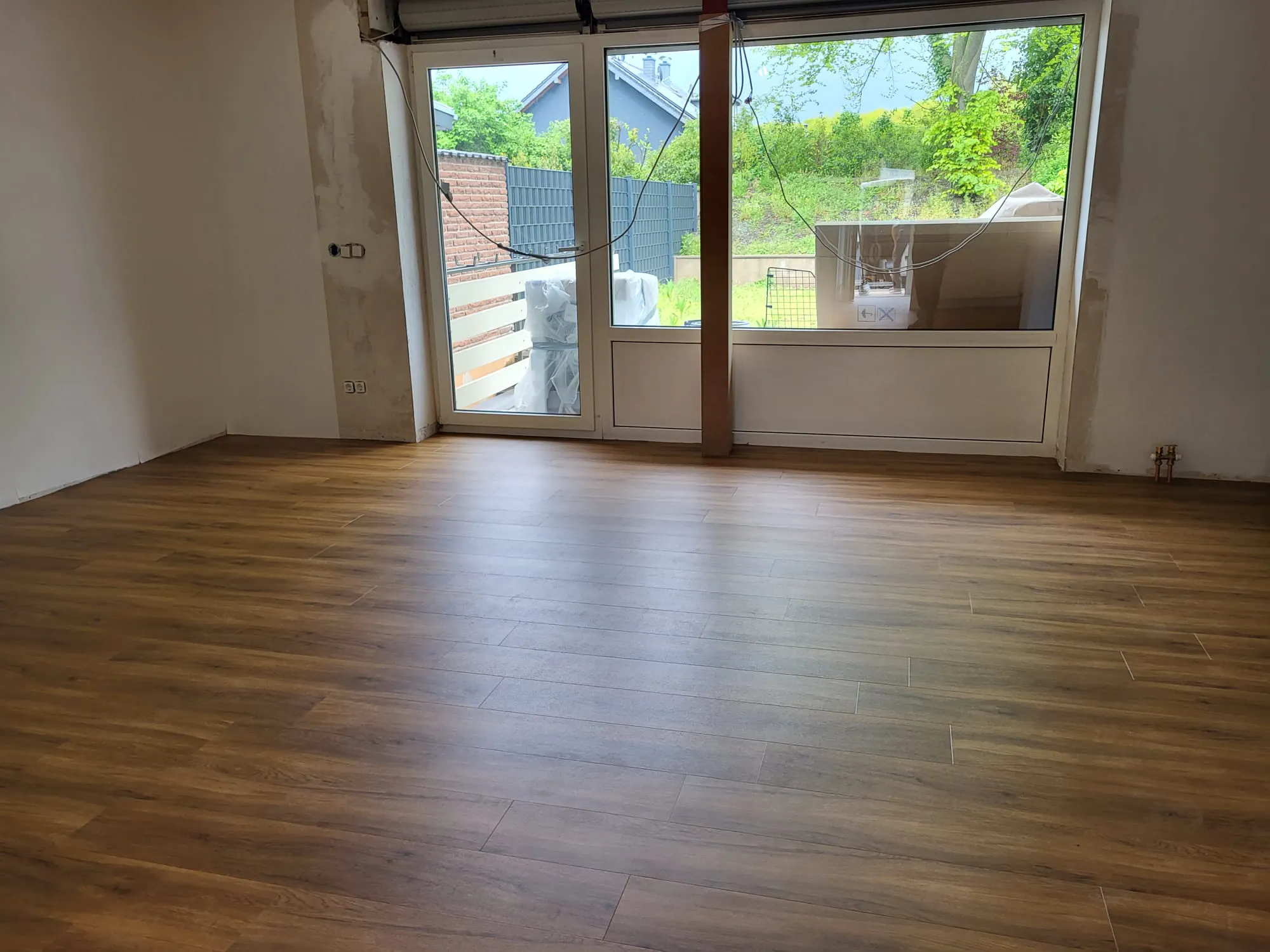Laminat verlegen – frisch verlegter Holzoptikboden in hellem Wohnraum vor großen Fenster- und Terrassentüren