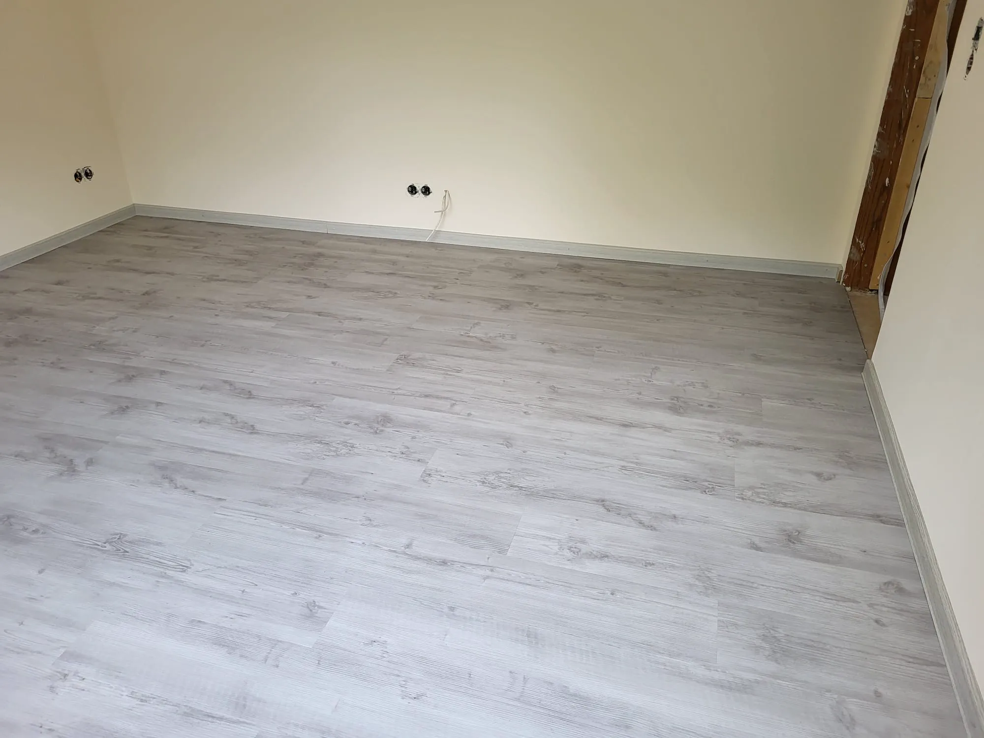 Neu verlegter hellgrauer Laminatboden mit Sockelleisten in renoviertem Raum – Laminat verlegen