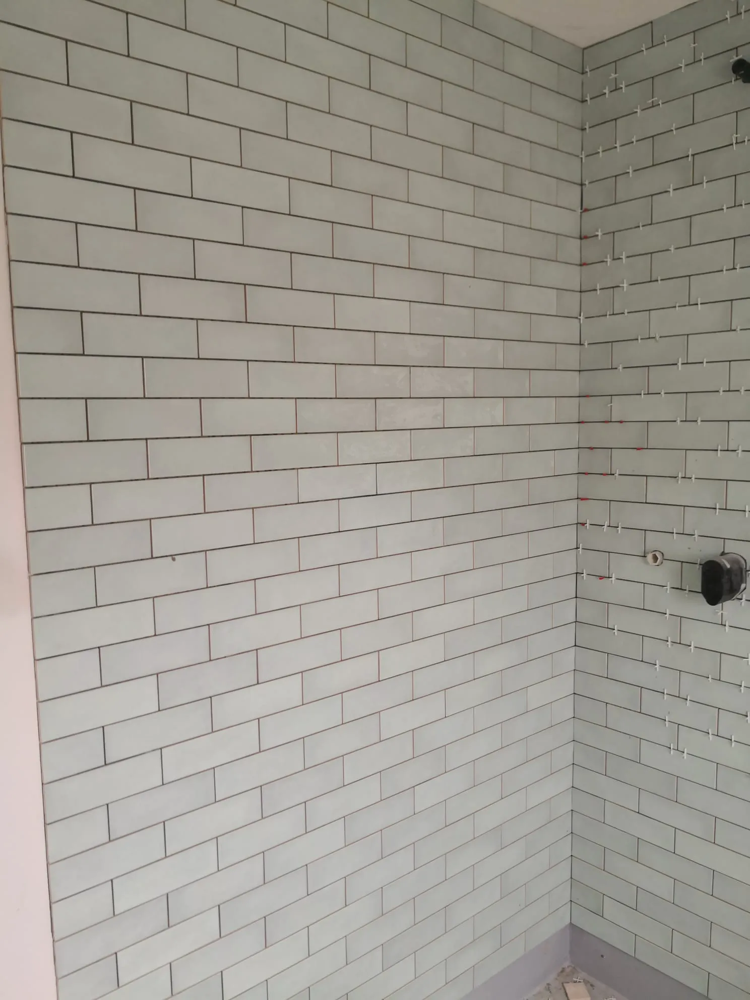 Ecke einer Dusche mit frisch verlegten weißen Wandfliesen und Fugenkreuzen, Fliesen verlegen