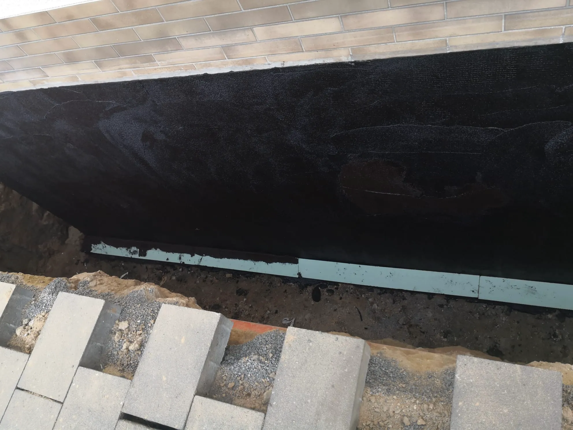 Ausgehobener Graben neben Klinkerwand mit Bitumenabdichtung und Dämmplatten für Kellerisolierung