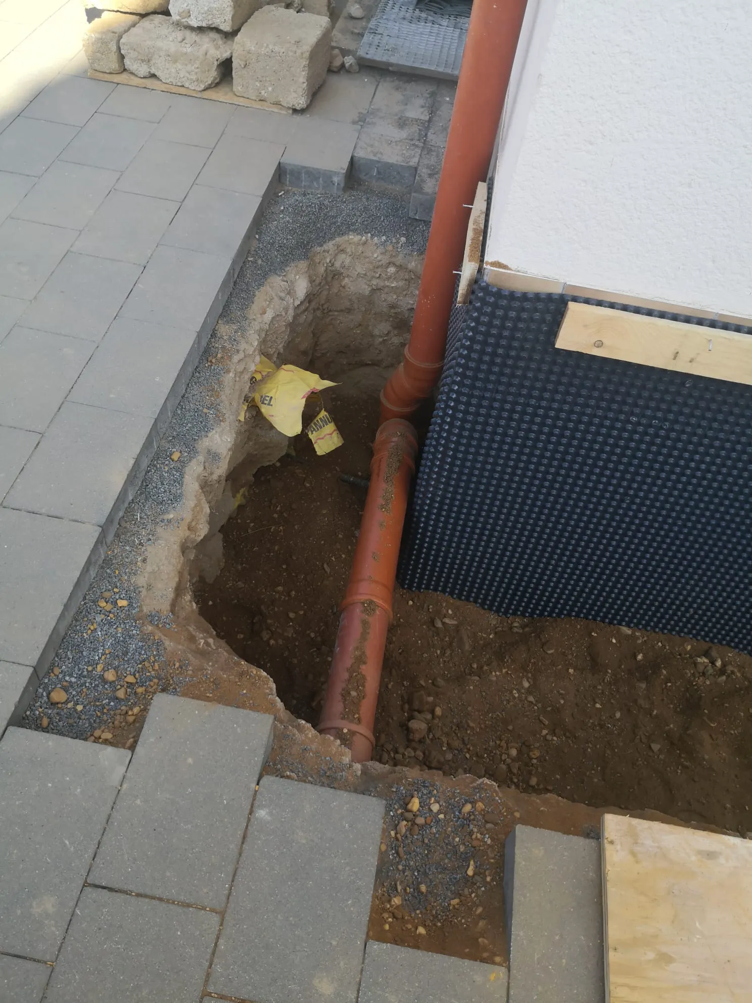 Baugrube am Hausfundament mit sichtbarem Drainagerohr bei Erdarbeiten