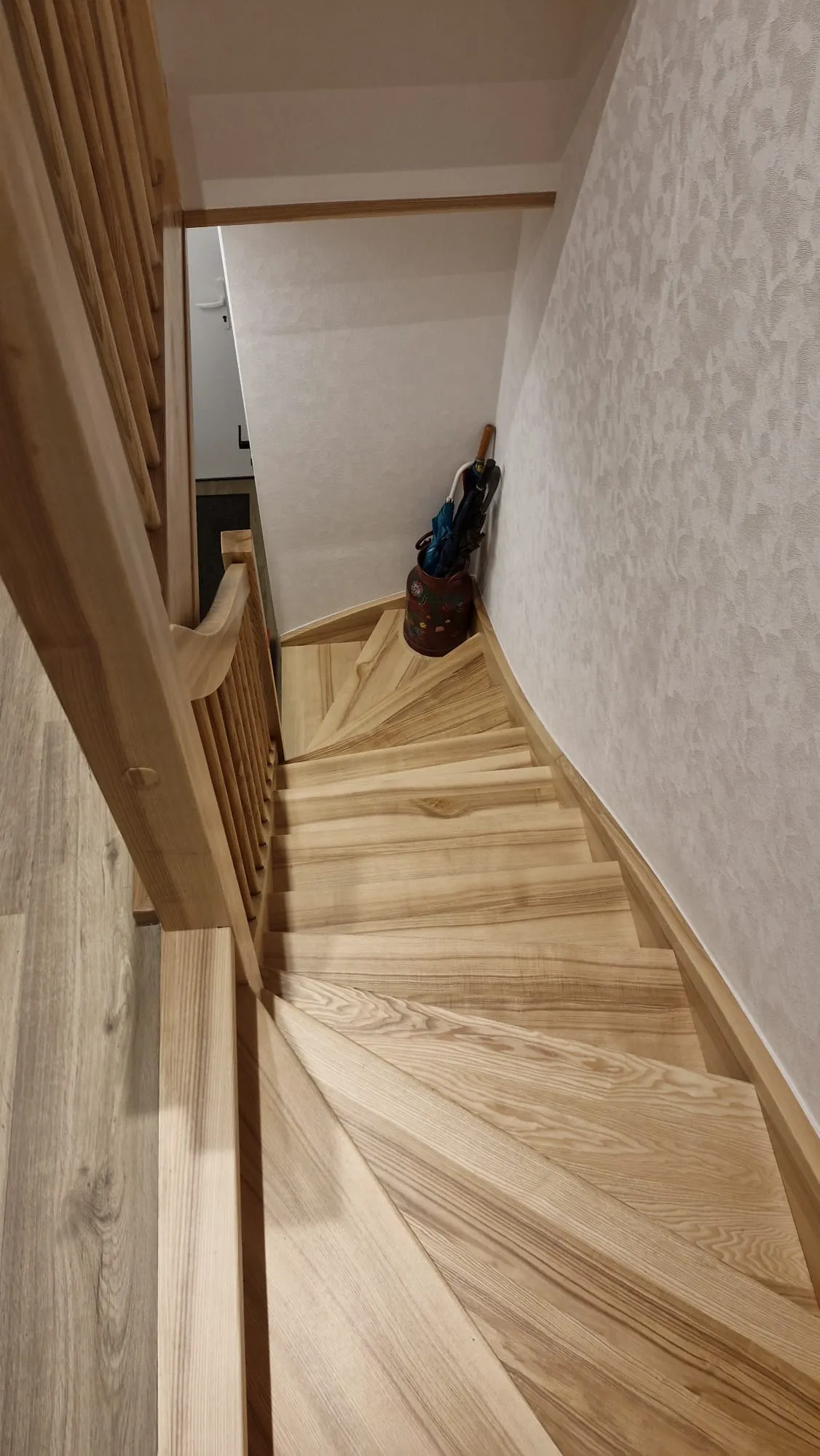 Geschwungene Holztreppe mit hellem Handlauf und einläufigen Stufen im Flur