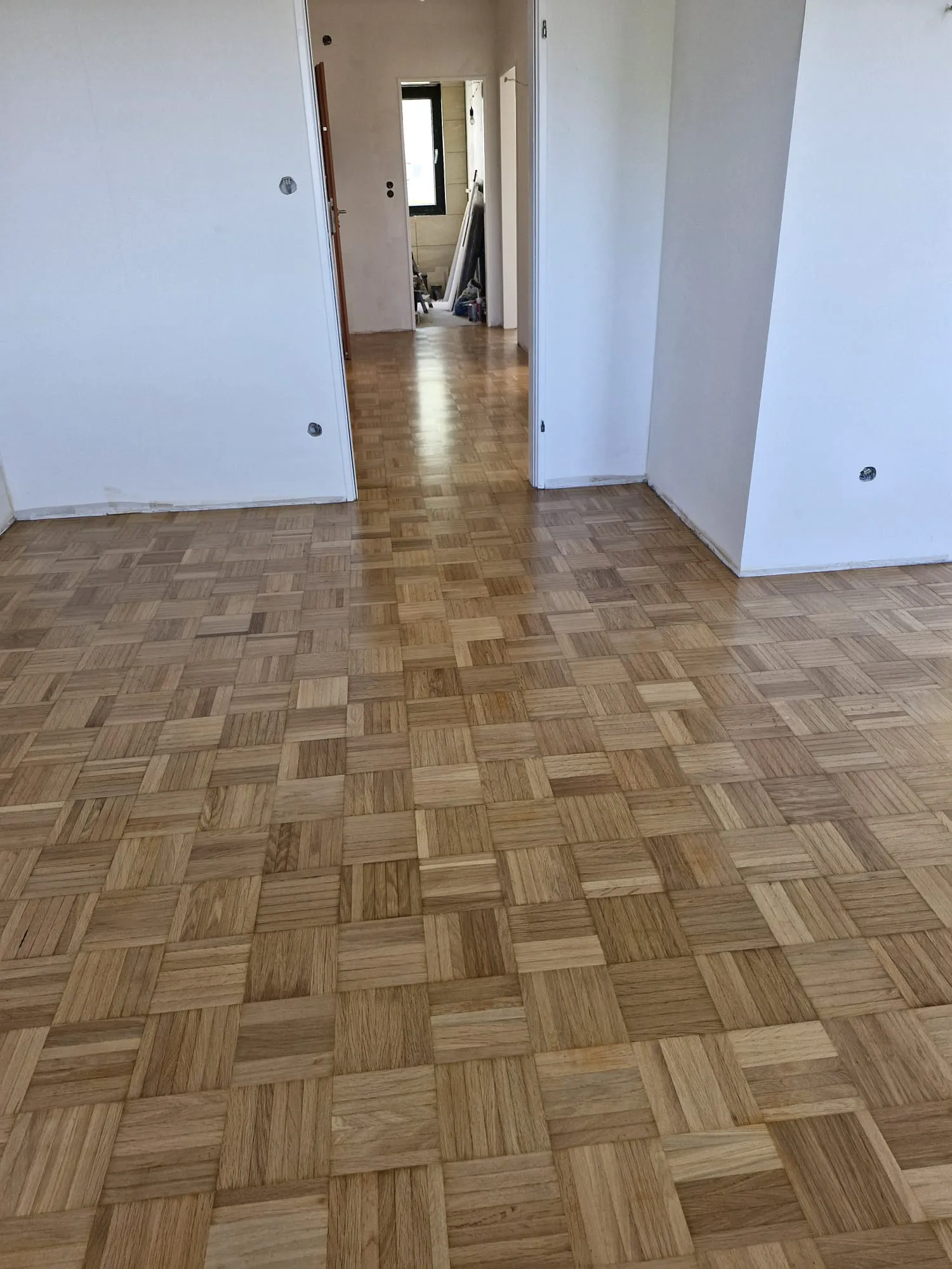 Heller, neu verlegter Parkettboden im leergeräumten Zimmer mit unvollendeten Wänden und Türen, Parkett verlegen