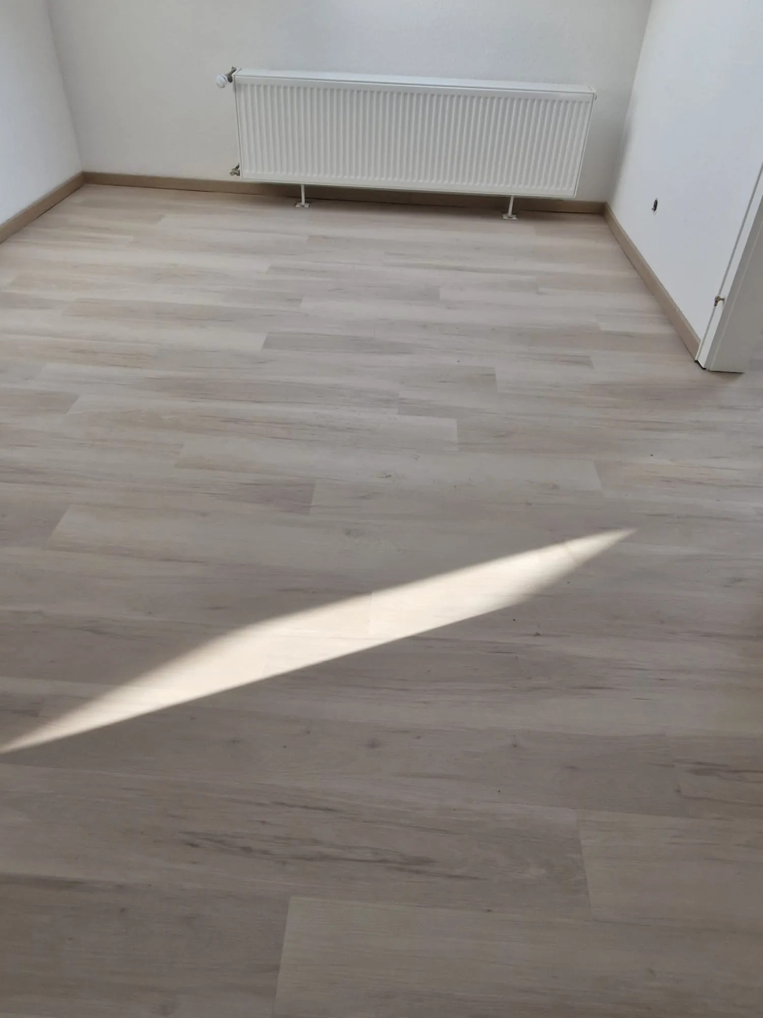 Raum mit frisch verlegtem Laminatboden (Laminat verlegen) in hellem Holzton und weißem Wandheizkörper