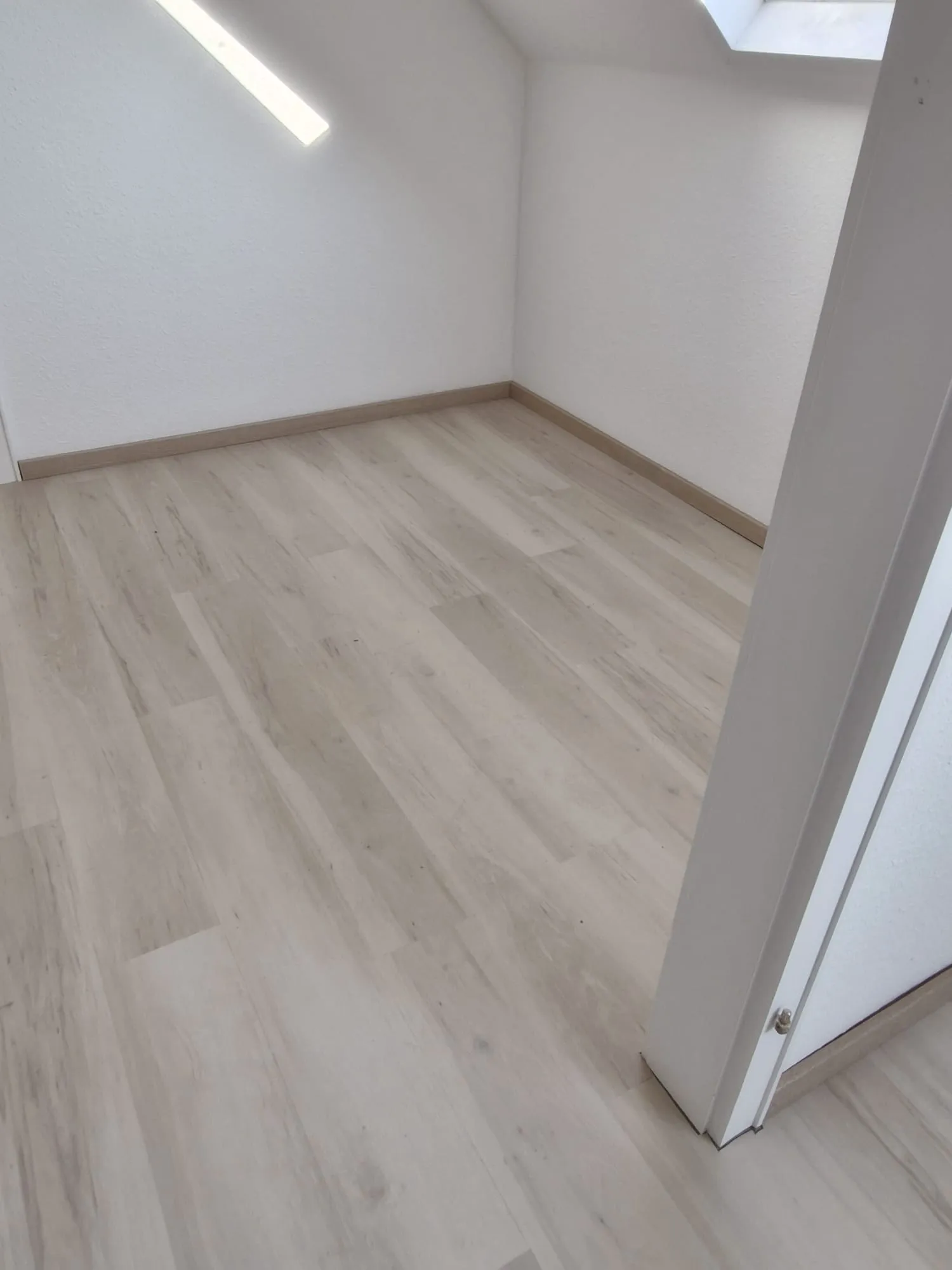 Heller Laminatboden in unmöbliertem Raum mit Dachschräge und weißen Wänden – Laminat verlegen