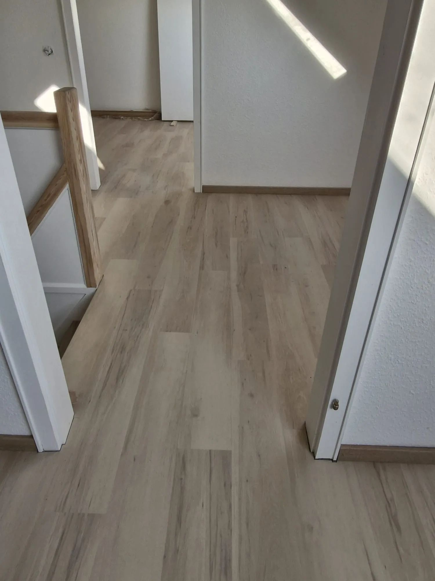 Laminat verlegen: heller Flur mit neuem Laminatboden, weiß gestrichenen Wänden und Holzgeländer