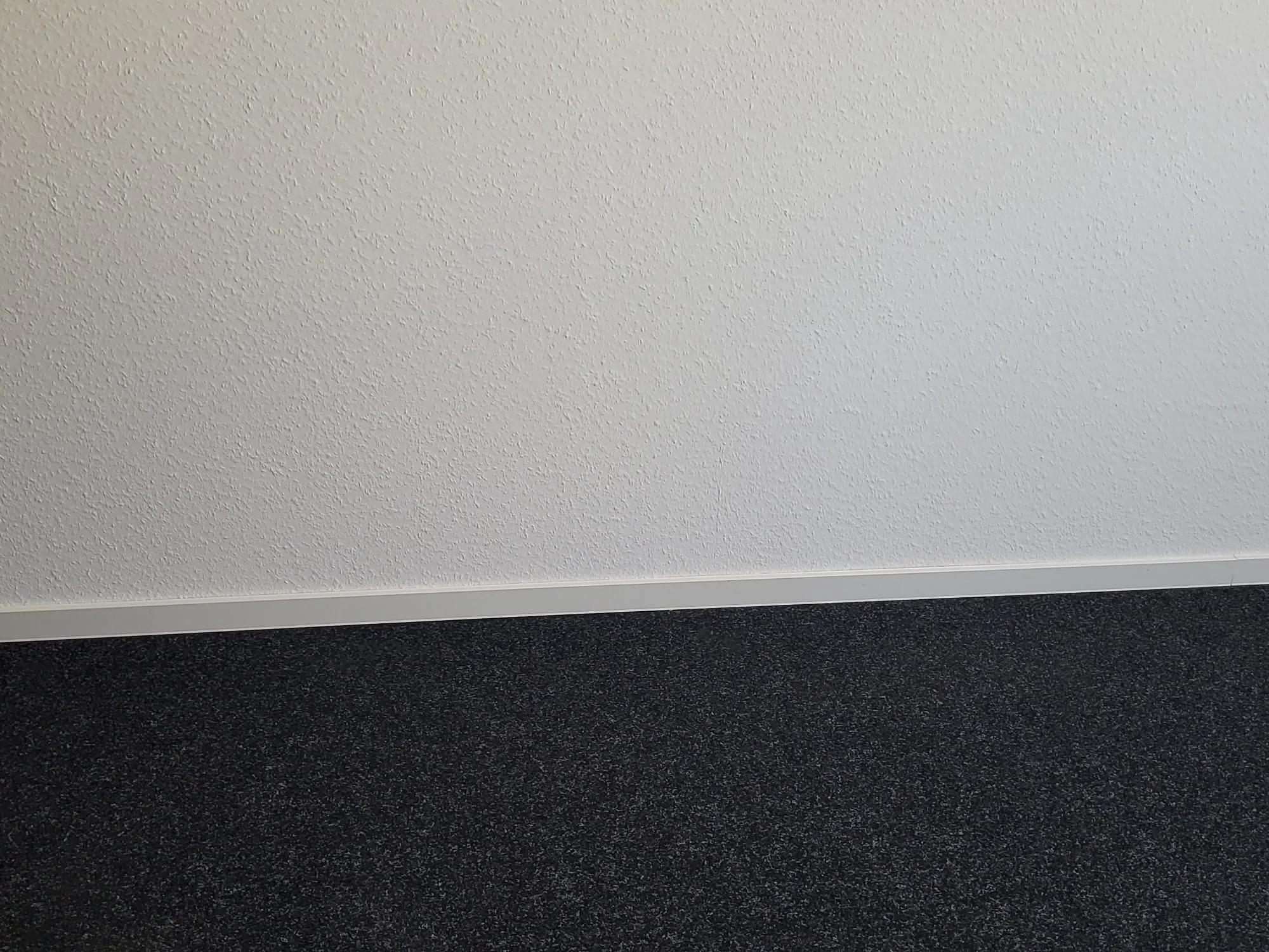 Grauer Teppichboden verlegen an weißer Wand mit Sockelleiste