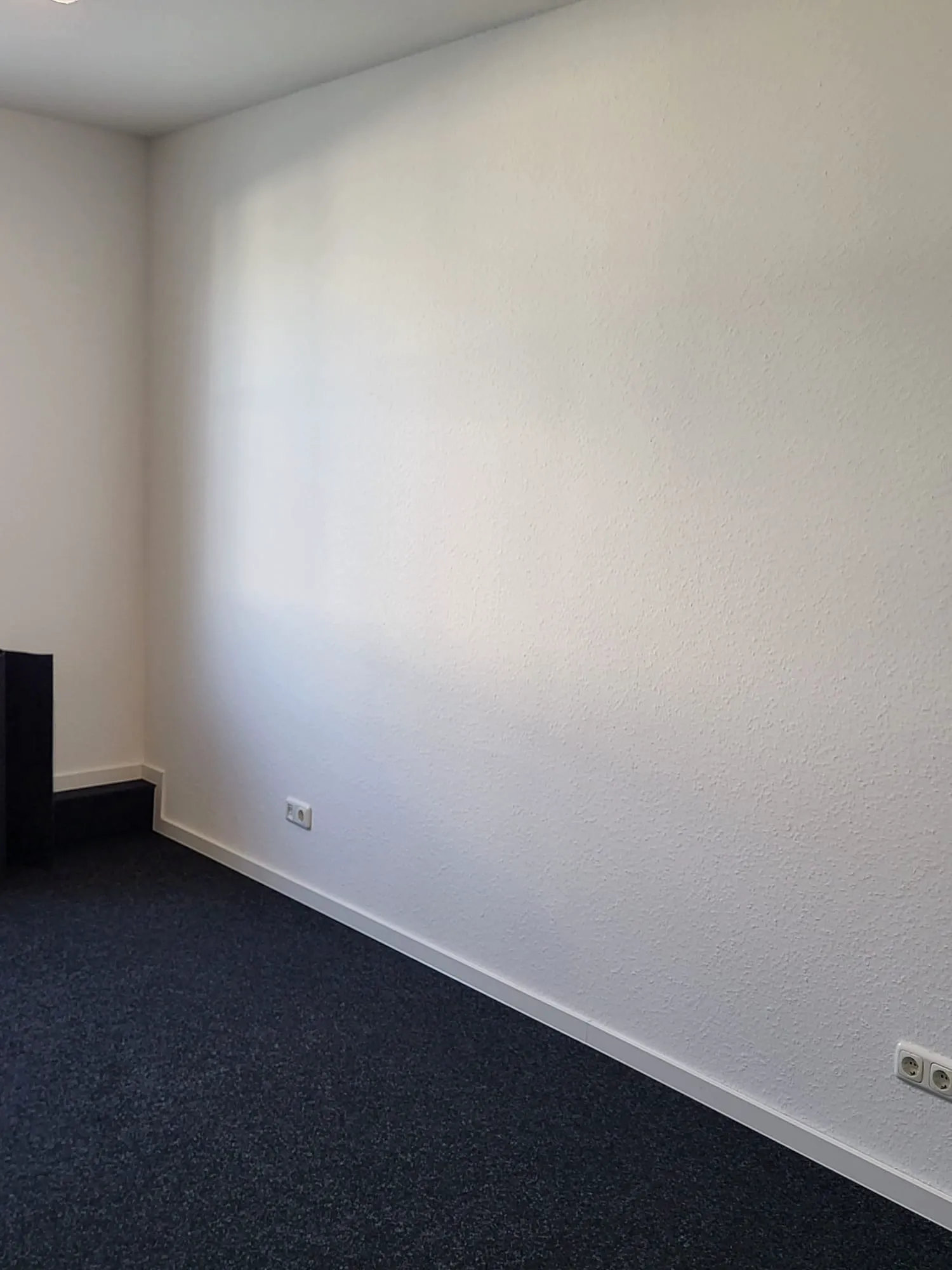 Raum mit weißer Wand, dunkelblauem Teppichboden und Steckdosen, Teppichboden verlegen