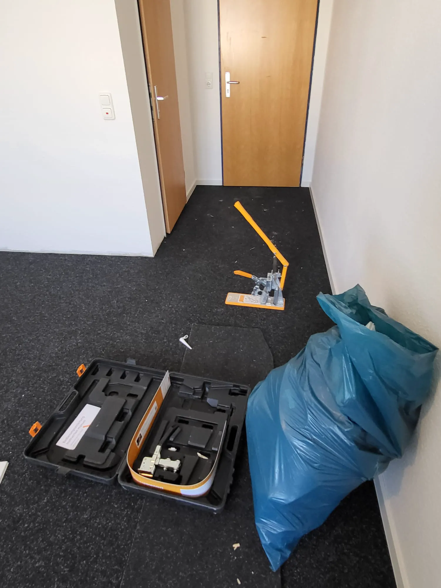 Handgeführter Bodenschneider, Werkzeugkoffer und Abfallbeutel auf vorbereitetem Boden für Laminat verlegen