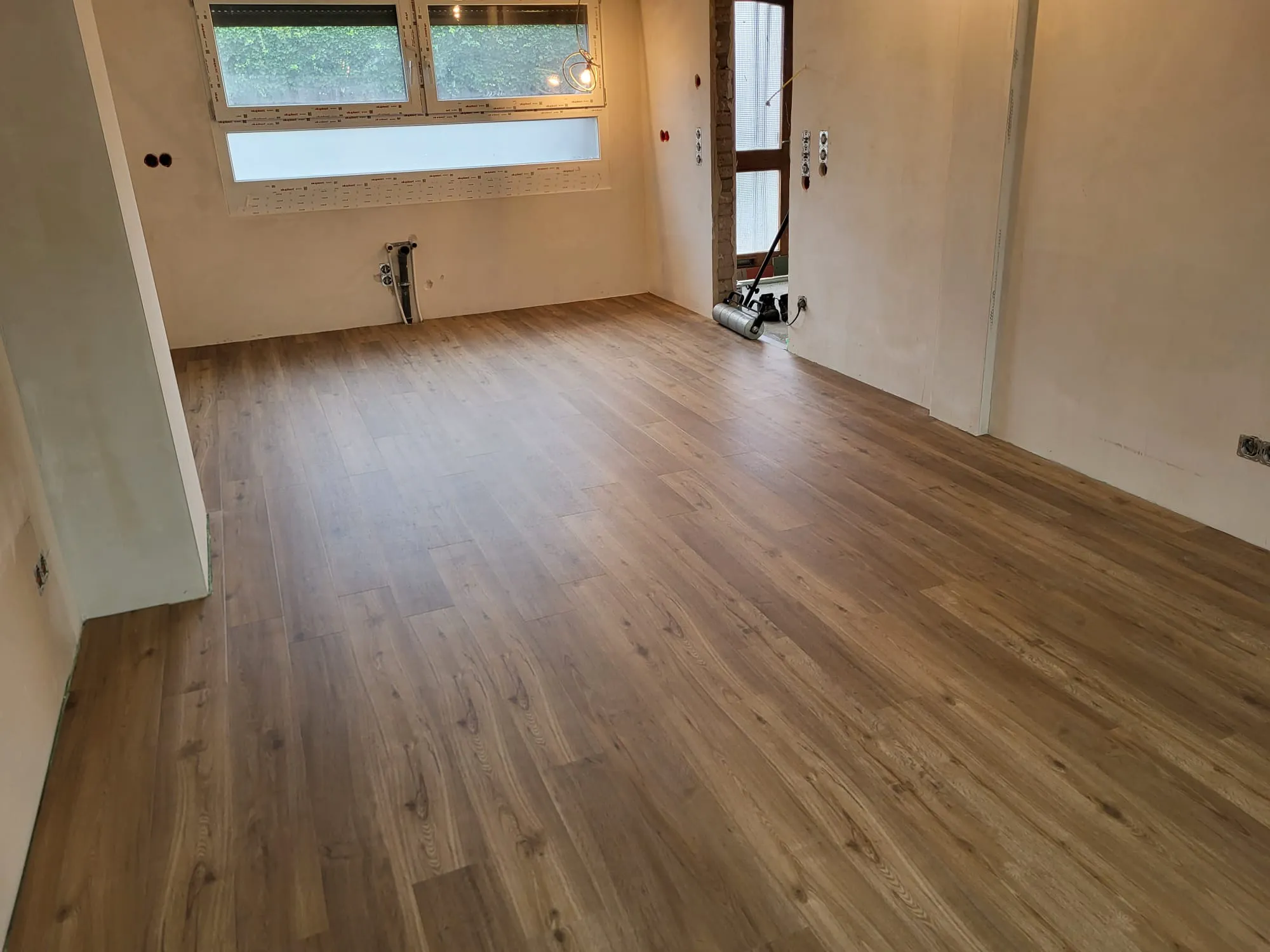 Innenansicht eines Raums mit frisch verlegtem Laminatboden, verputzten Wänden und Fenstern