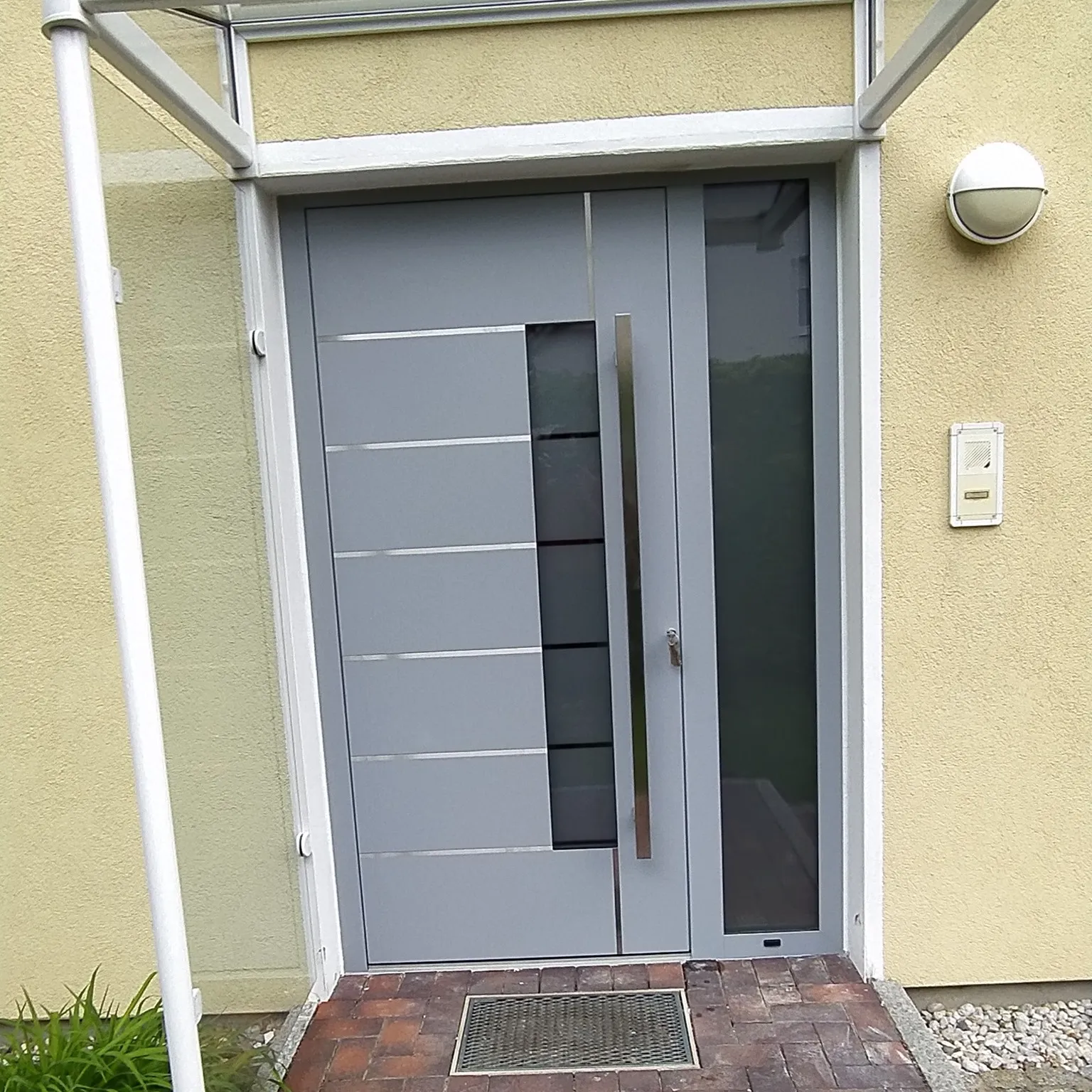 Moderne graue Außentür mit Seitenteil aus Glas, langem Griff und Vordach