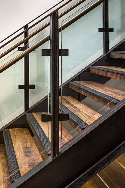 Vierläufige Holztreppe mit Glasgeländer und schwarzem Metallrahmen im modernen Innenbereich