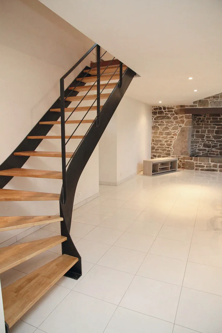 Moderne Stahltreppe mit Holzstufen und schlichtem Metallgeländer in hellem Raum mit Fliesenboden und Natursteinwand