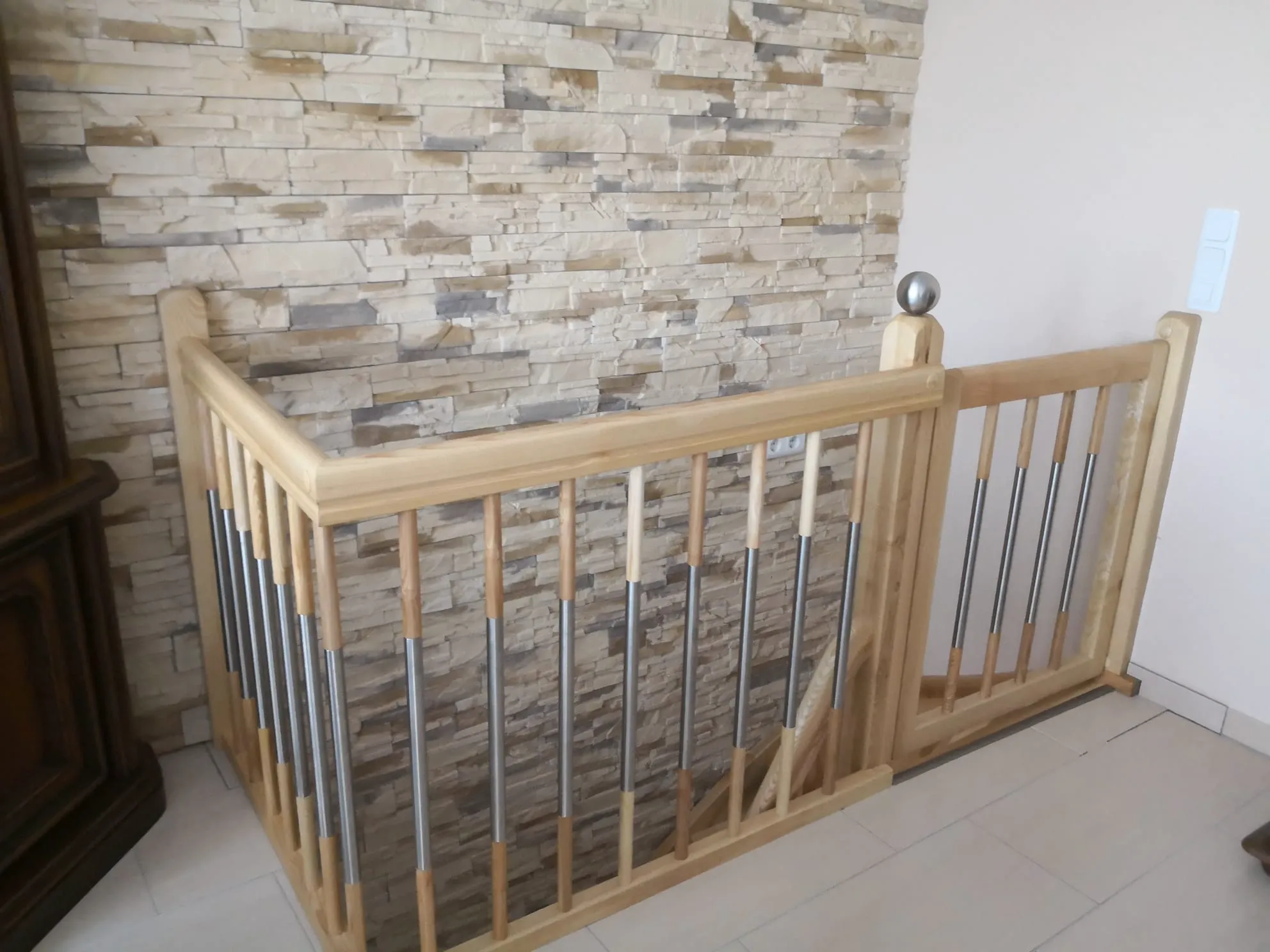 Innenbereich mit Holzgeländer und Edelstahlstäben an Treppenöffnung vor Steinwand