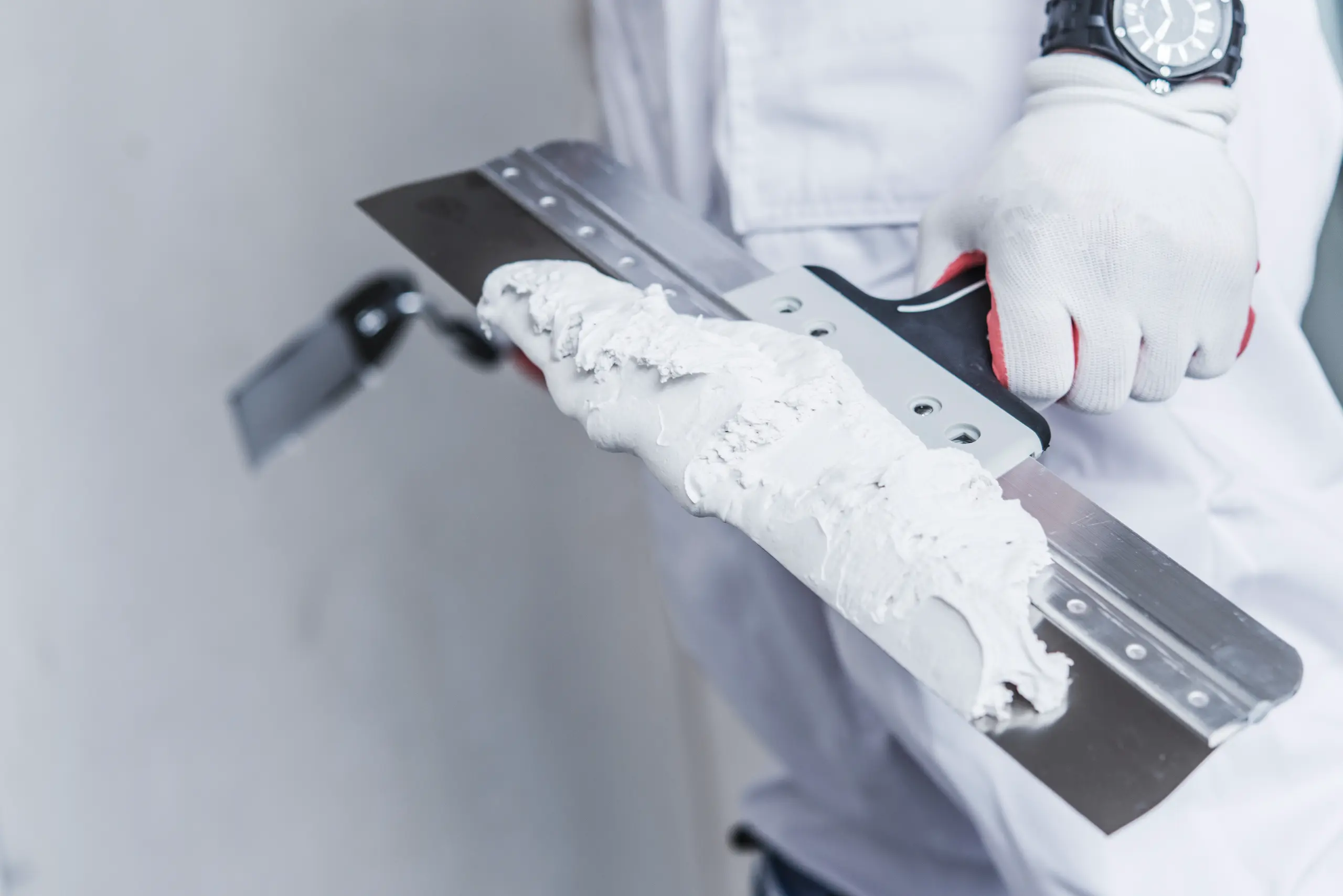 Putzarbeiten: Arbeiter mit Handschuhen trägt weiße Spachtelmasse mit einer Edelstahlkelle auf Wand auf